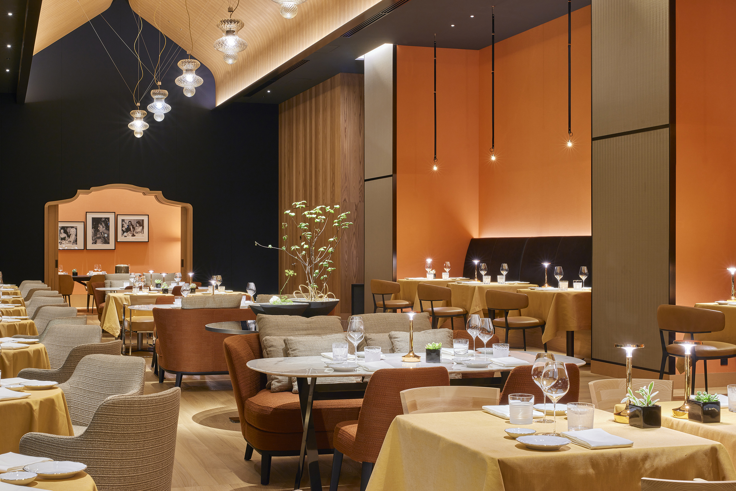 A high-ceiling restaurant decorated in shades of orange and black with sleek dining tables and hanging pendent lights