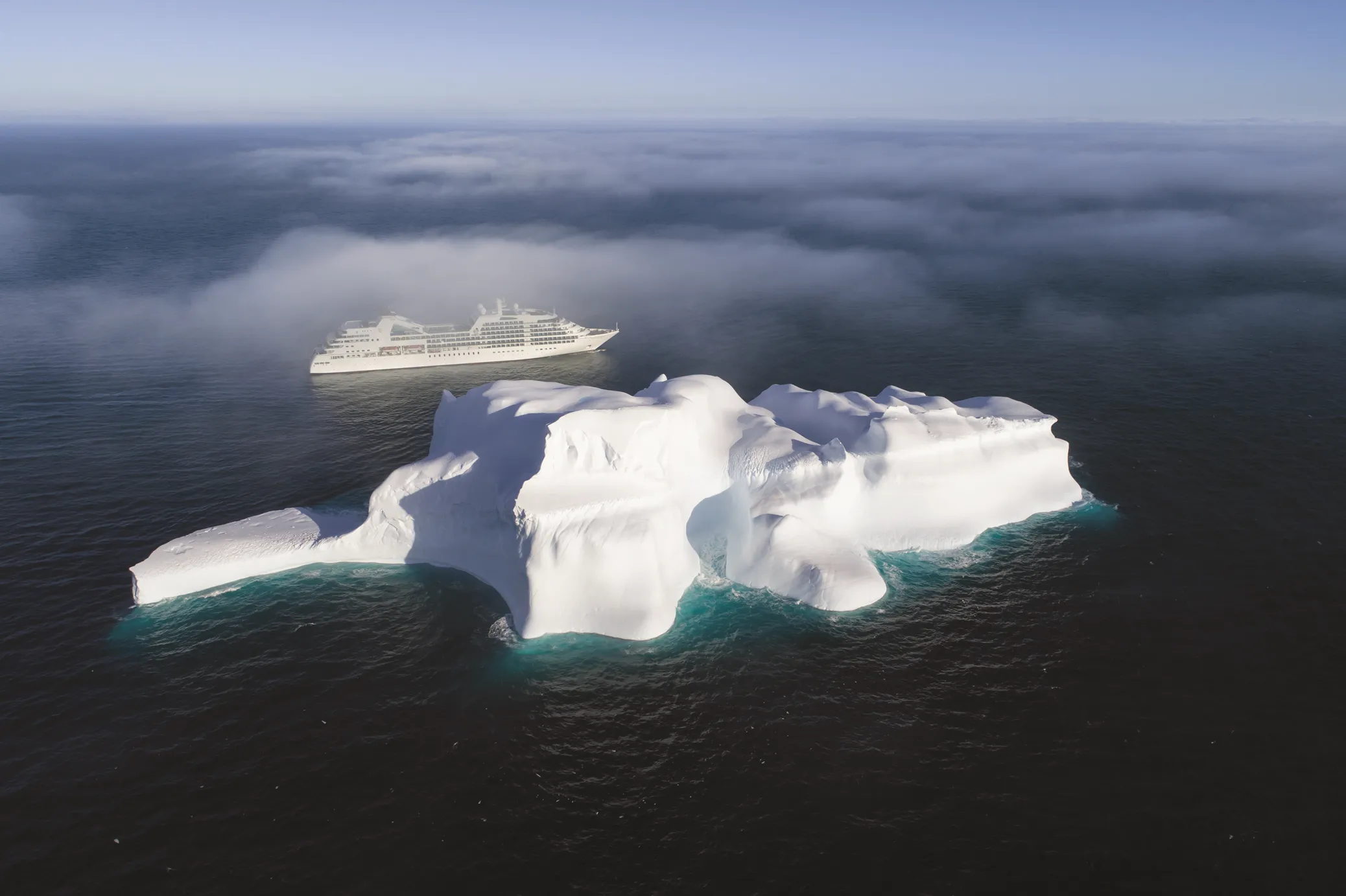 Cruise ship sailing near a large iceberg in the ocean under a cloudy sky.