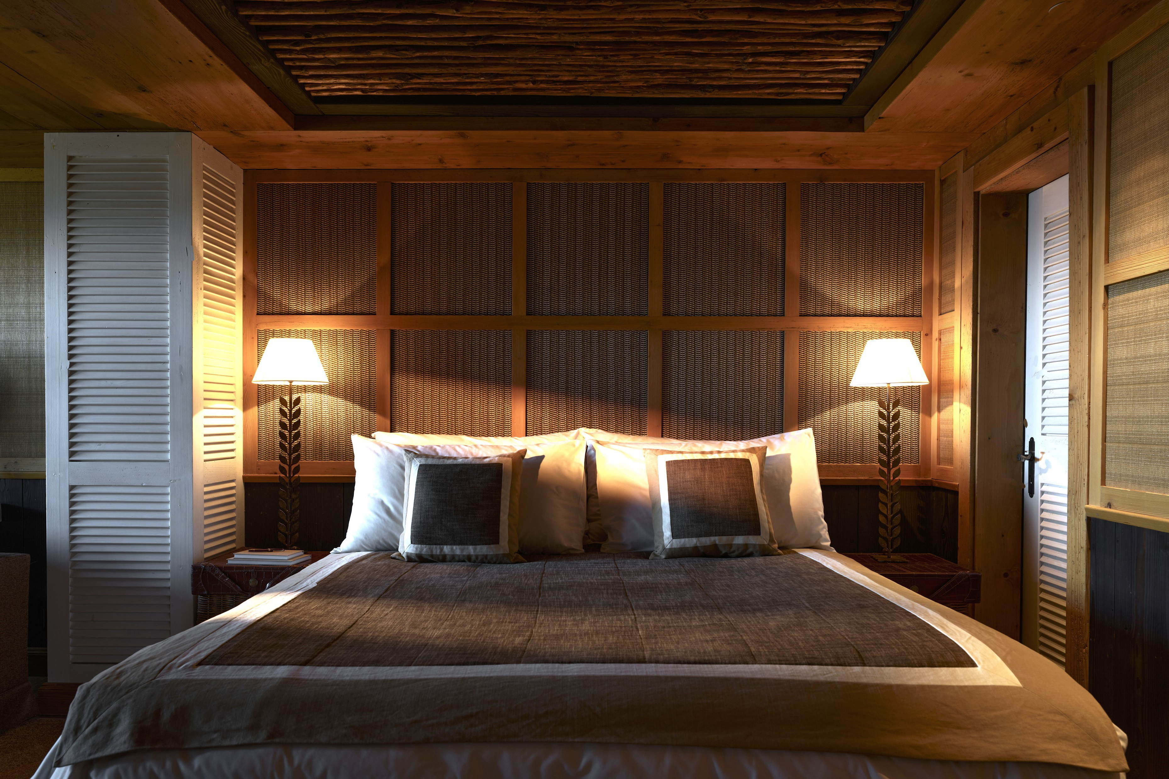 A double bed with patterned covers flanked by lamps with a decorative wall behind