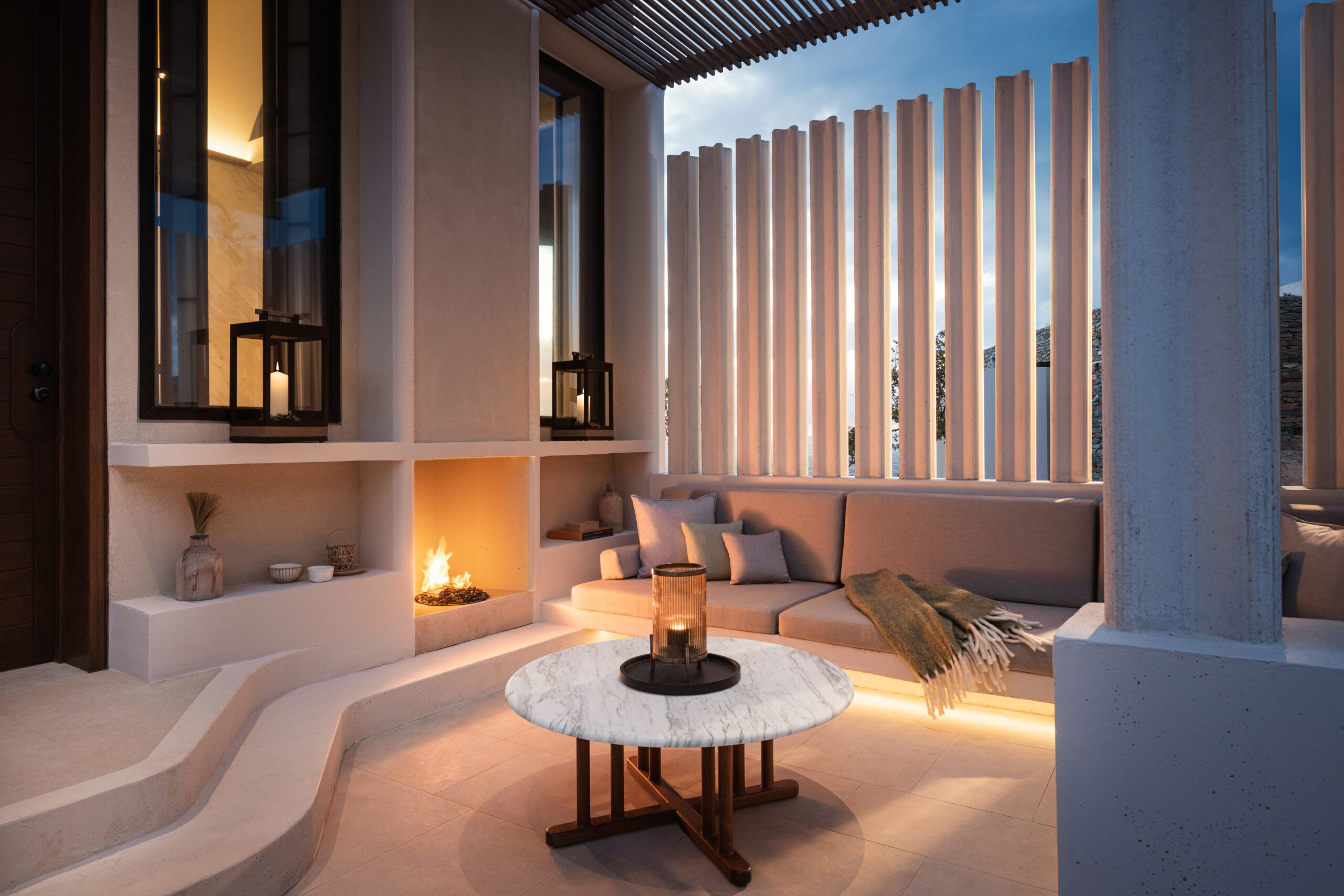 Carved stone fireplace seating area of Kea Island villa with lit fire and cushions