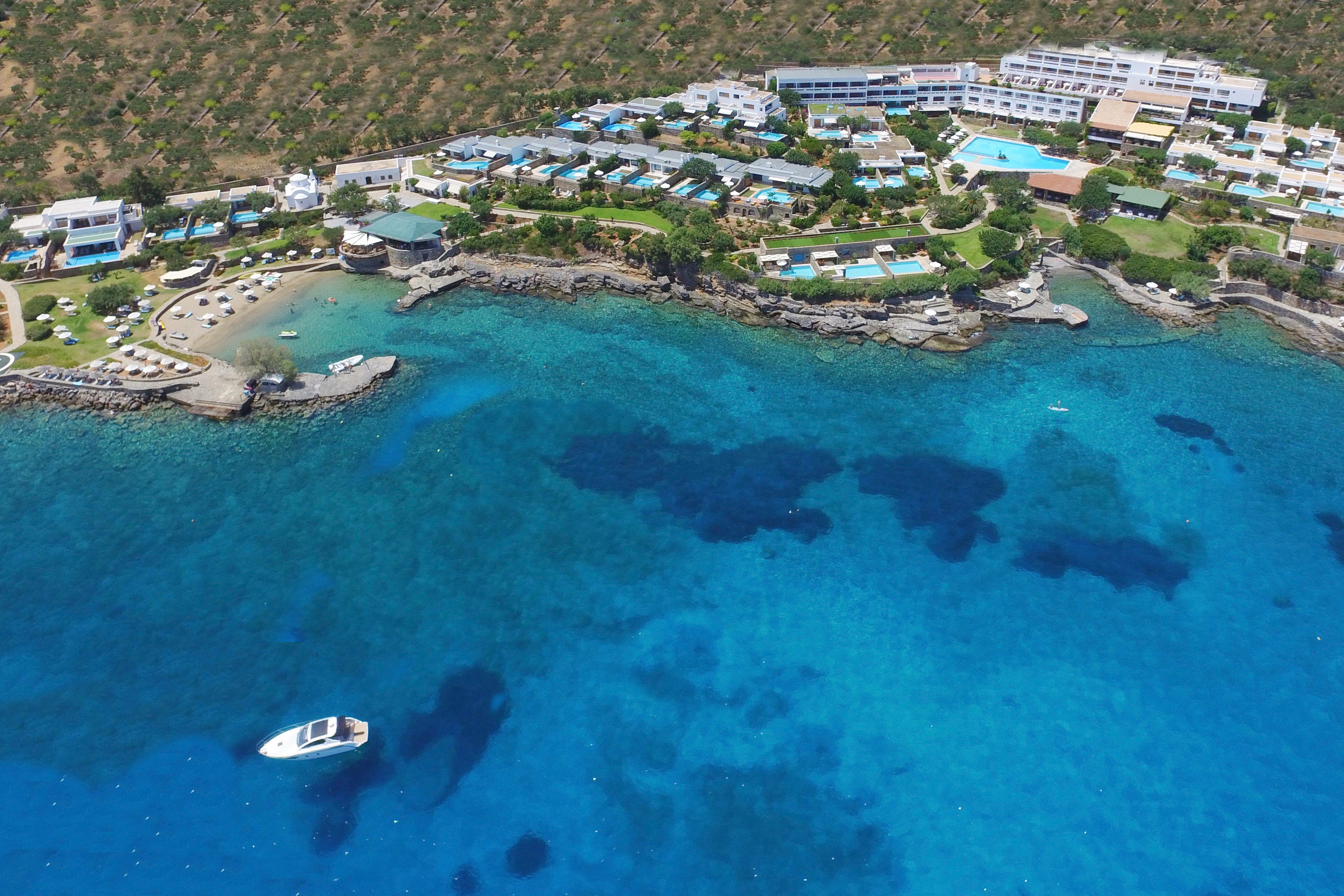 View from above of Elounda Mare hotel with white yacht anchored just offland in the water