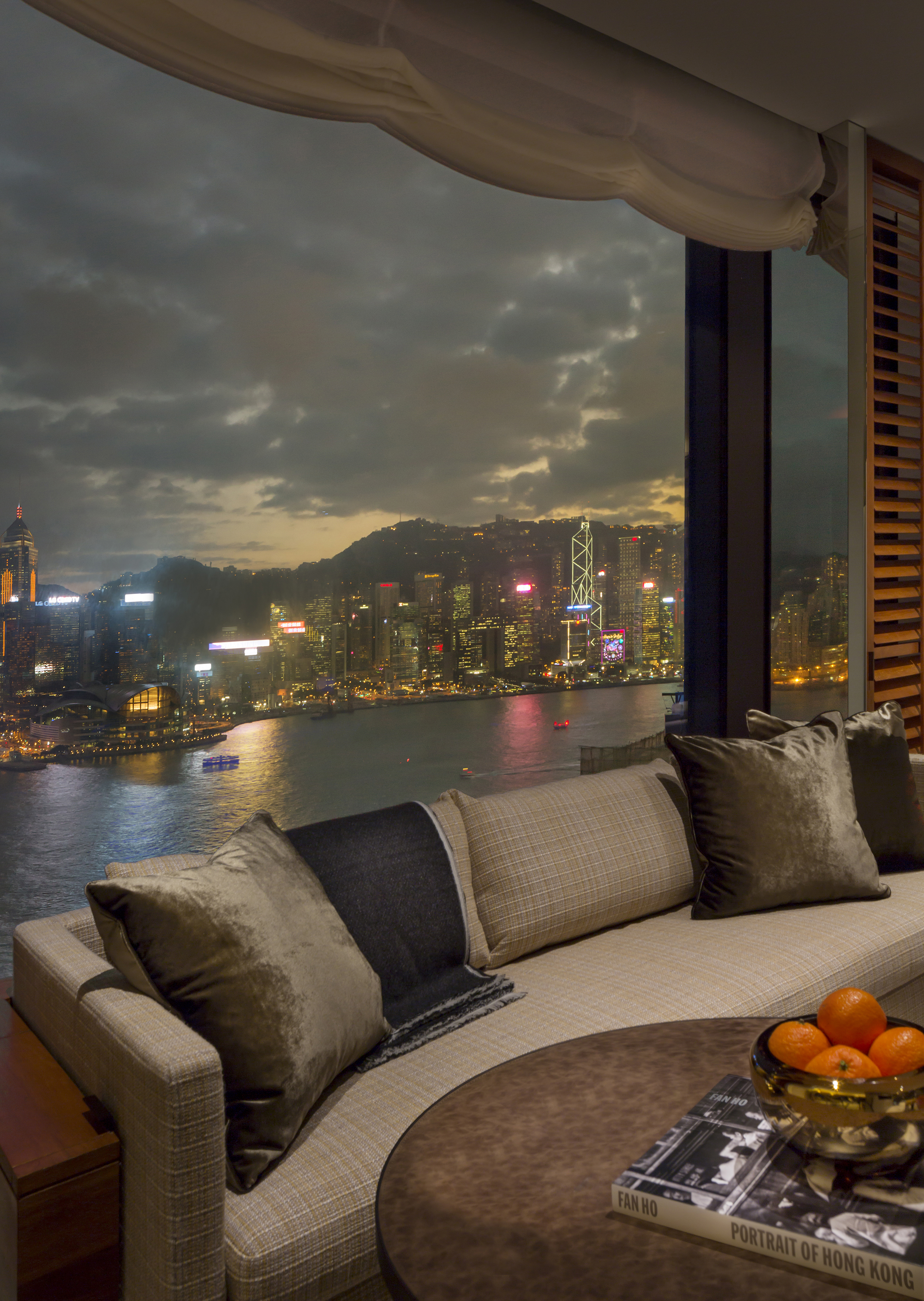 Part of a sofa and table in a suite at Rosewood Hong Kong set before a large window with city views