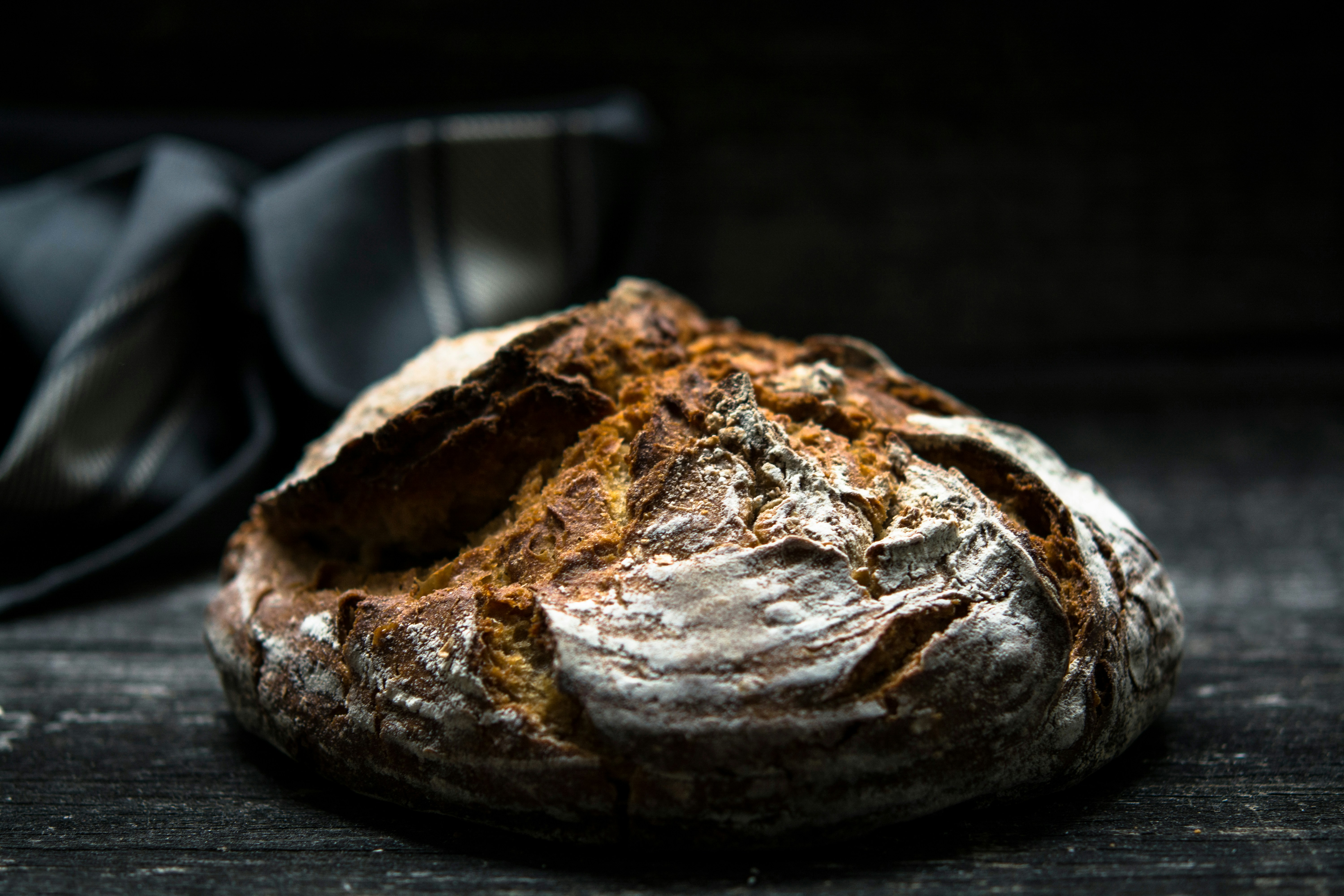 Load of crusty bread on black table with dark dish cloth behind