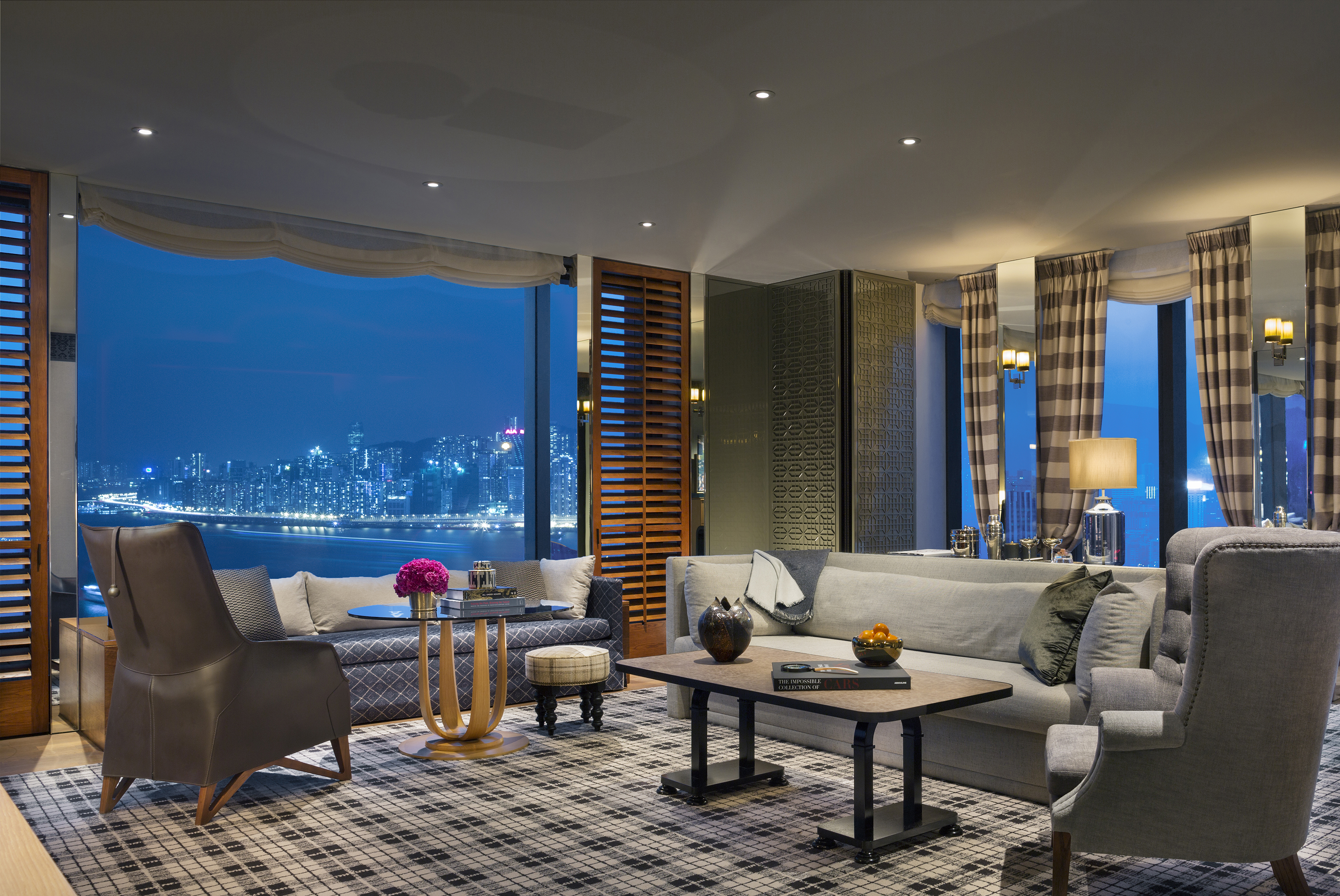 The lounge of a Harbour Corner Suite featuring comfy sofas, coffee tables with vases and patterned soft furnishings with city views out the window
