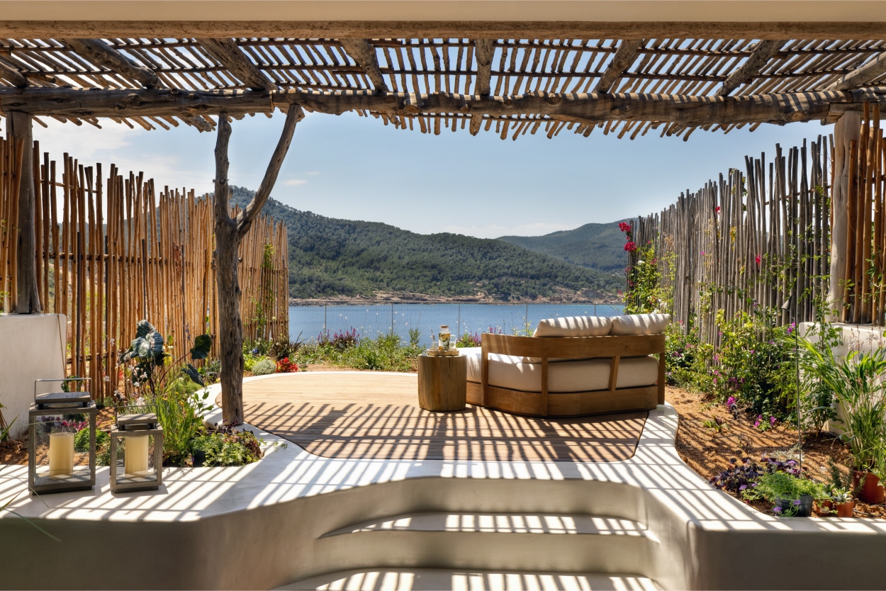 Shaded outdoor patio with a wooden pergola, overlooking mountains and a body of water.