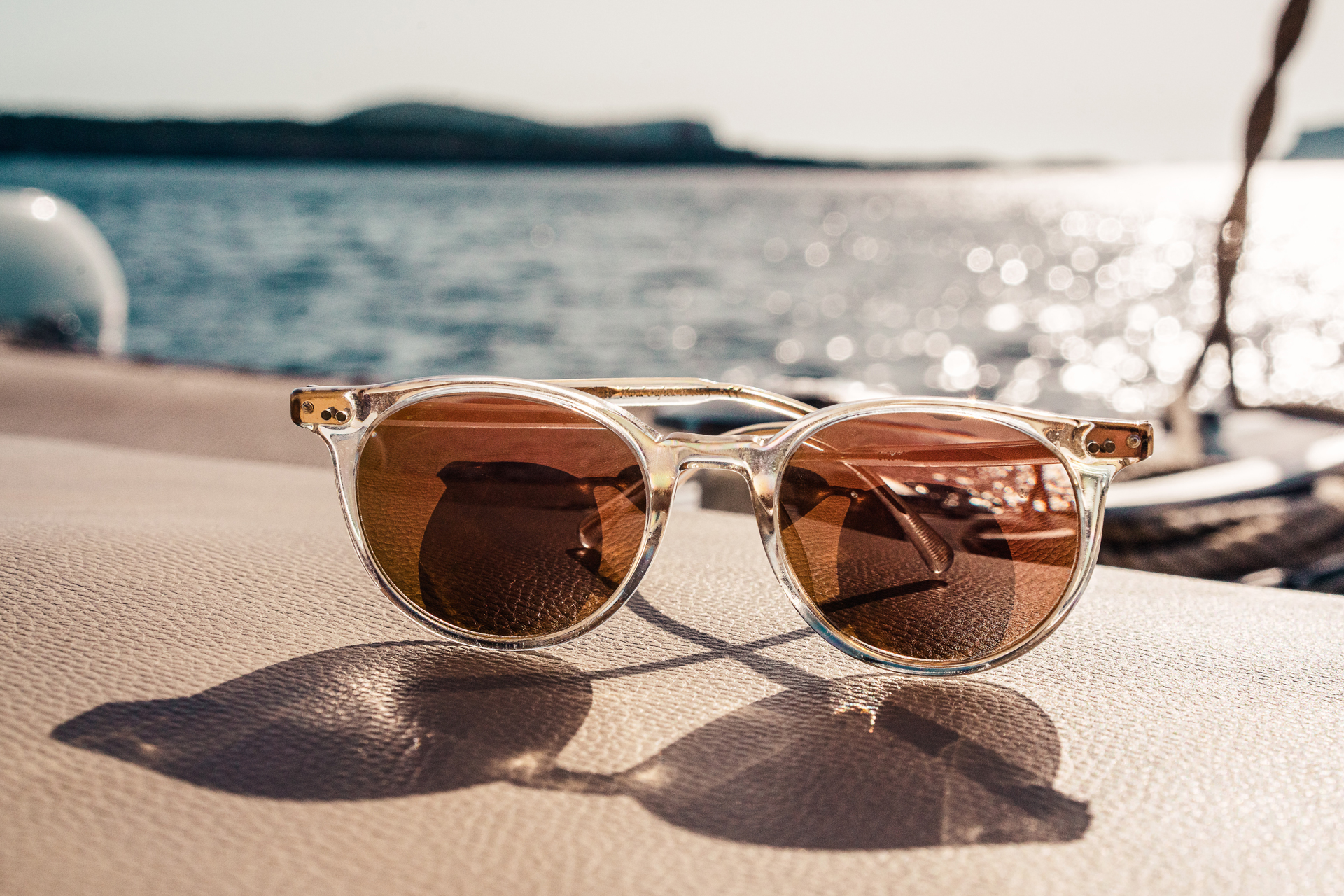 White framed brown lens sunglasses with the sea in the background