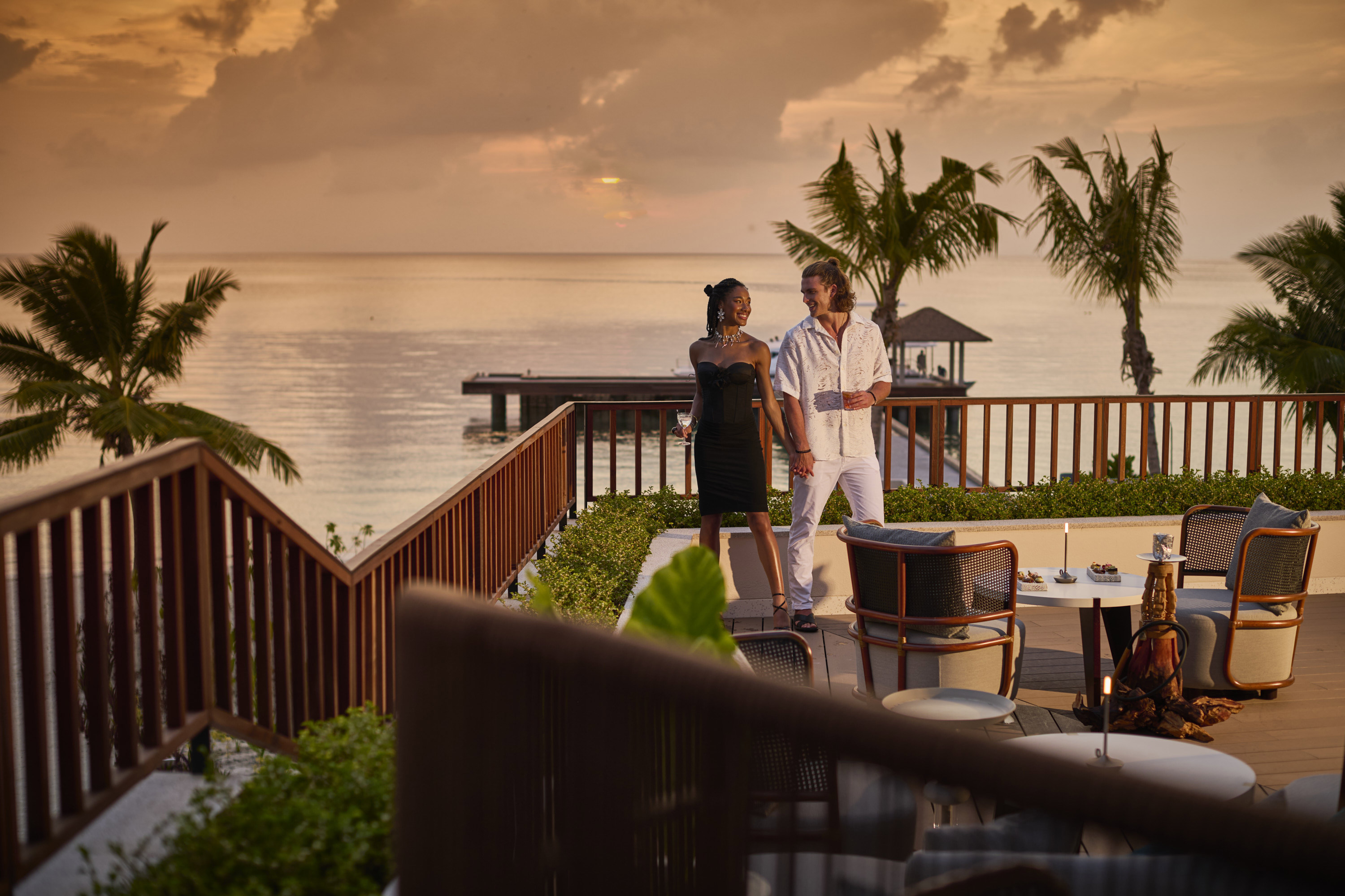 Couple in black and white standing on the terrace of the bar at sunset