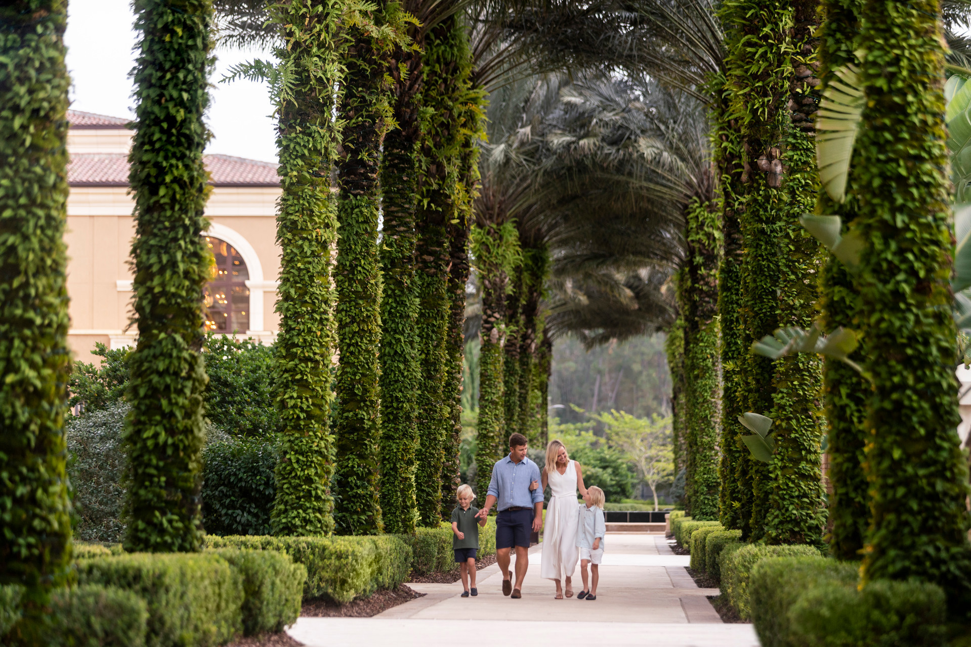 Family of four walking together through a palm-lined path at Four Seasons Resort Orlando at Walt Disney World® Resort
