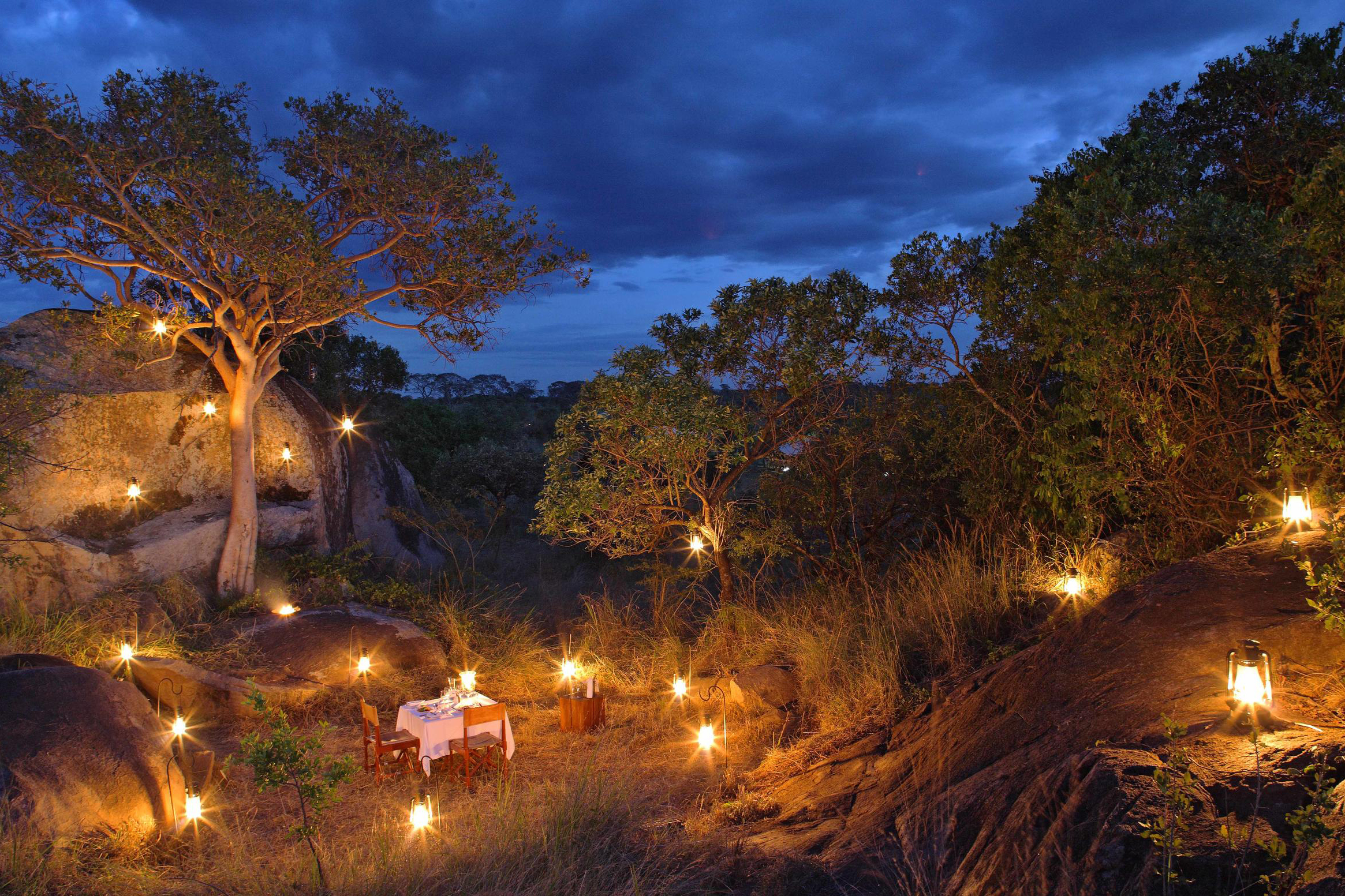 A private dining table set up in the middle of a rock formation surrounded by trees and candles