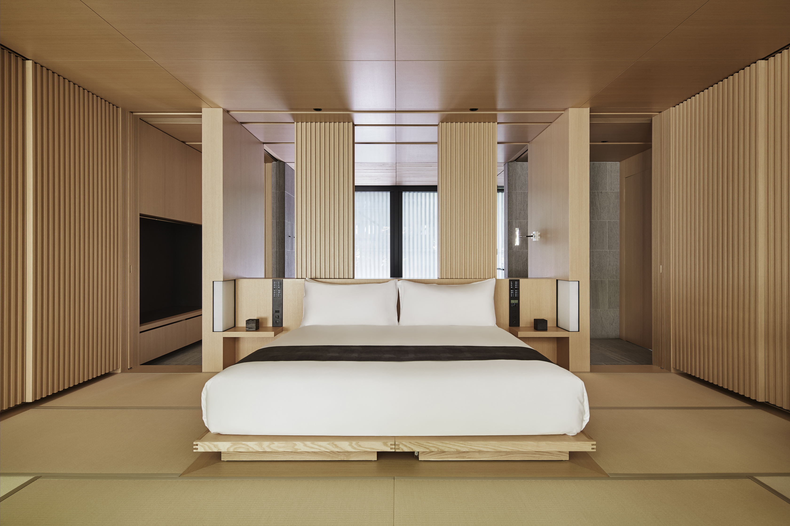 A comfy bed in a suite at Aman Kyoto surrounded by pale wood decor 