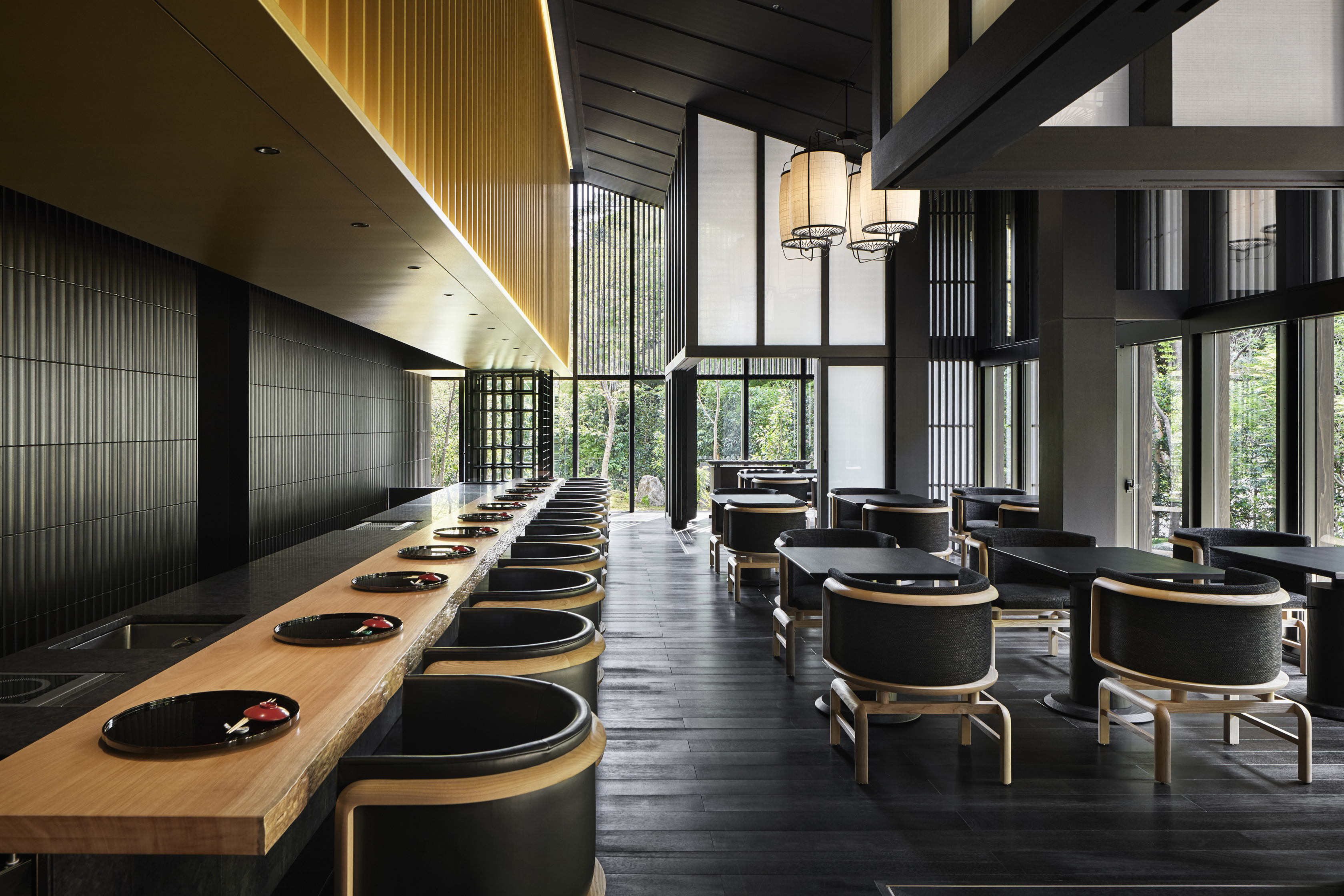 Taka An Restaurant at Aman Kyoto featuring a sushi bar and dining tables in black and pale wood beneath high traditional ceilings