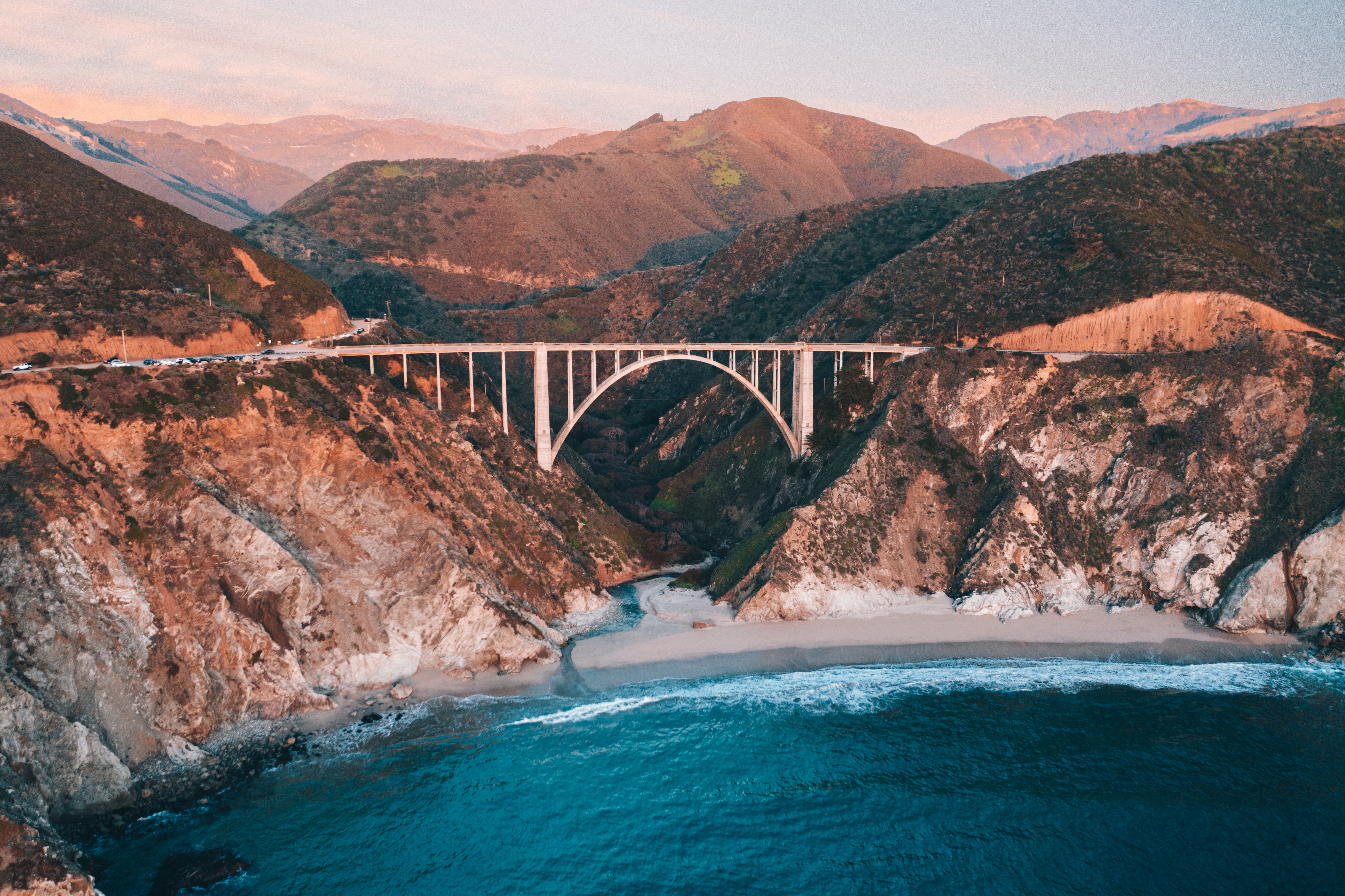 A wide angle of Bixby Bridge in Big Sur stretching across the mouth of a valley that flows into the sea