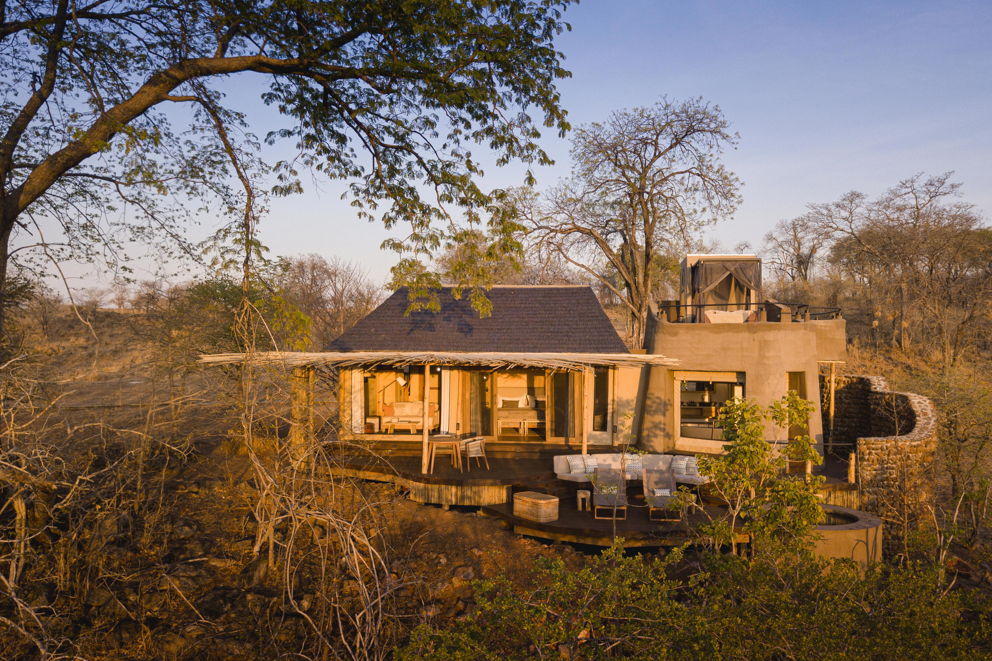 Exterior view of a luxurious lodge at Puku Ridge Camp, featuring an open-air deck with seating areas, surrounded by dry trees and bushland under a clear sky