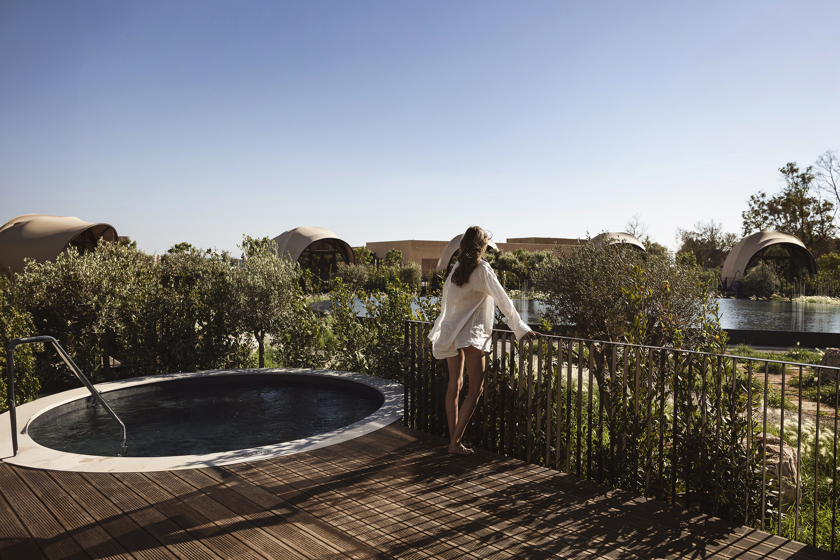 Woman dressed in loose white shirt standing on private terrace with plunge pool