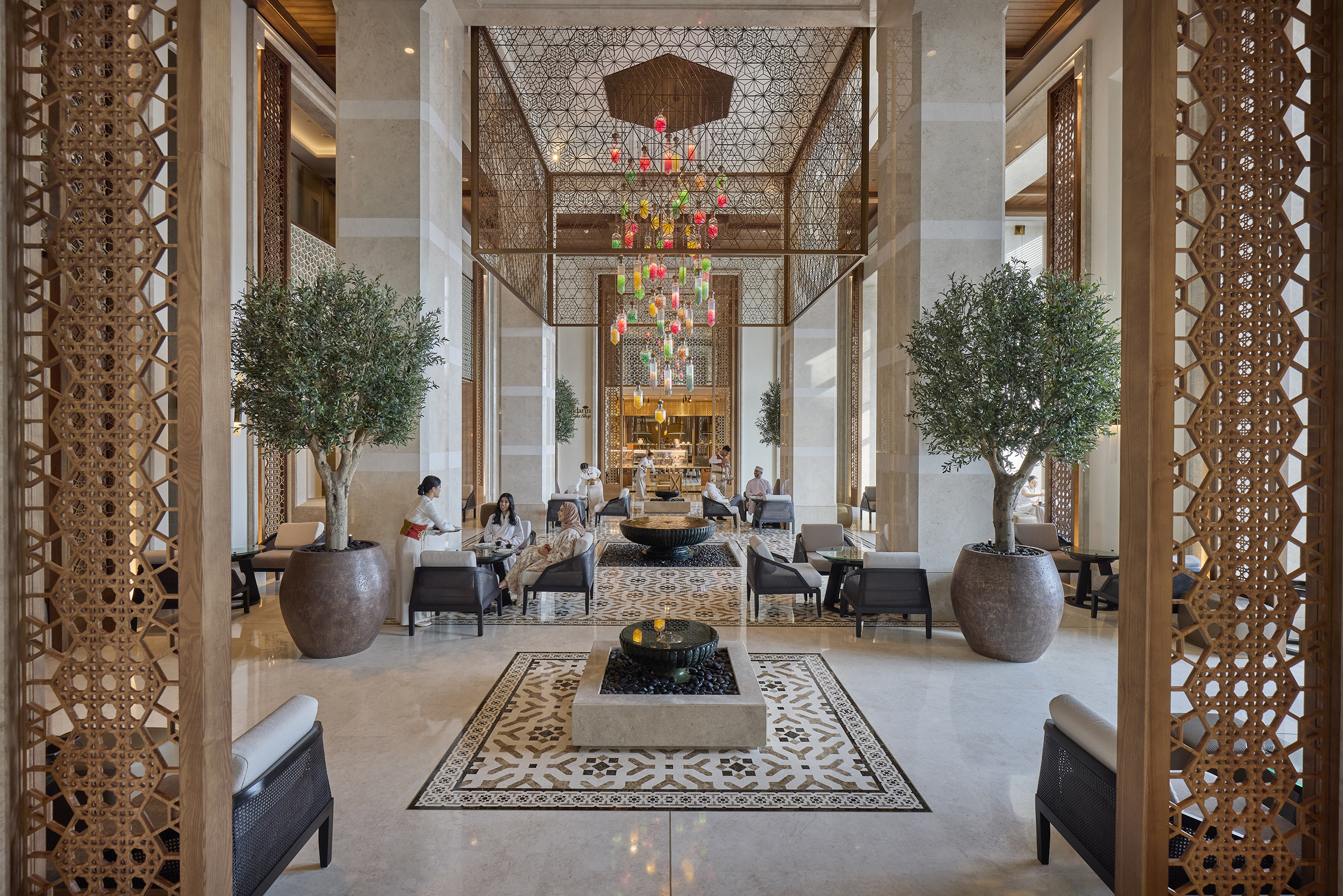 Sawa Lounge in the lobby of Mandarin Oriental Muscat with guests having afternoon tea beneath a large sculptural chandelier by two olive trees