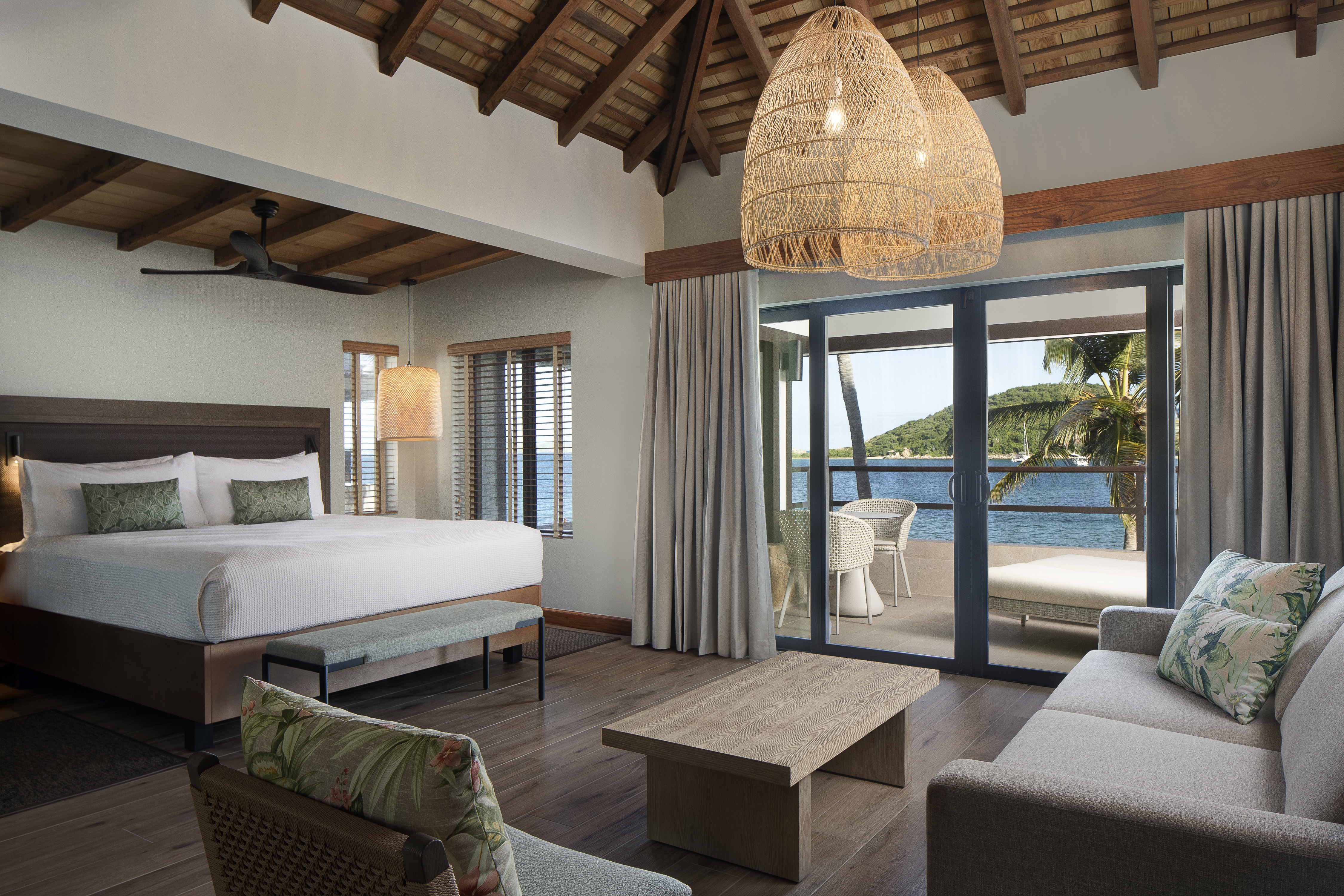 Bedroom with comfy bed and sofa area with a coffee table below a wooden beamed ceiling with sliding doors out to a patio