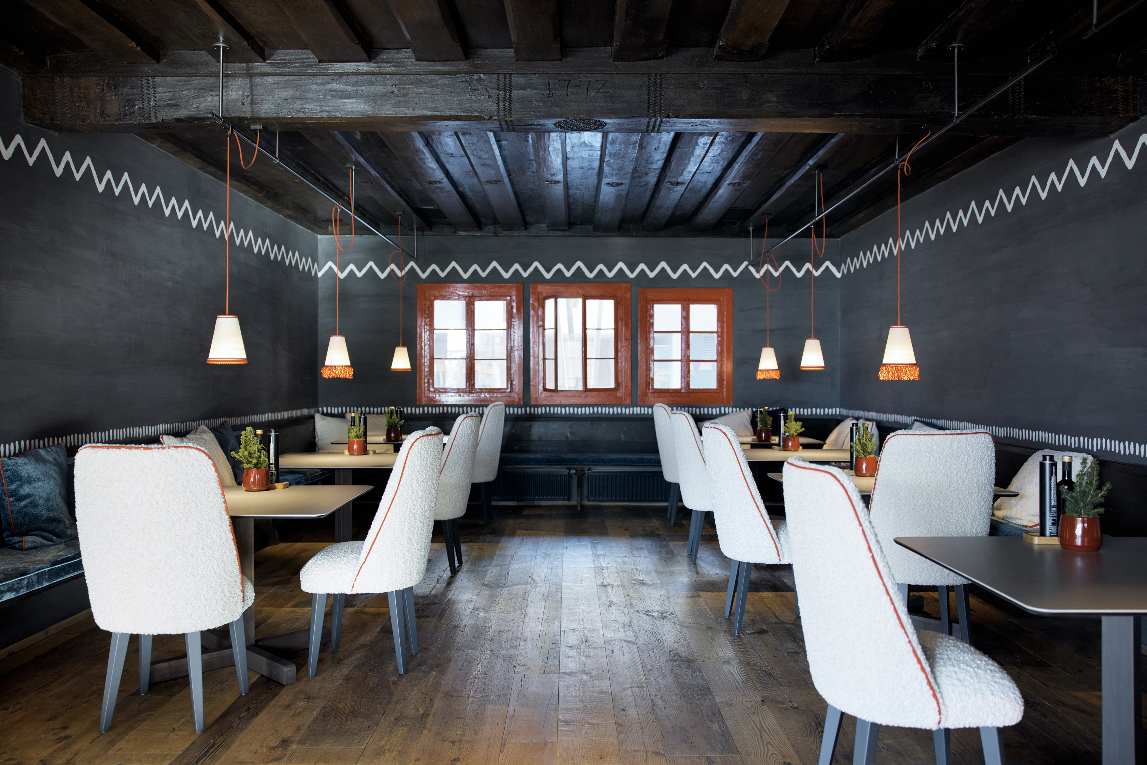 Cozy and stylish Trattoria Dell'alpe restaurant interior with dark walls, wooden floors, and a zigzag pattern along the wall, featuring comfortable seating and pendant lighting.