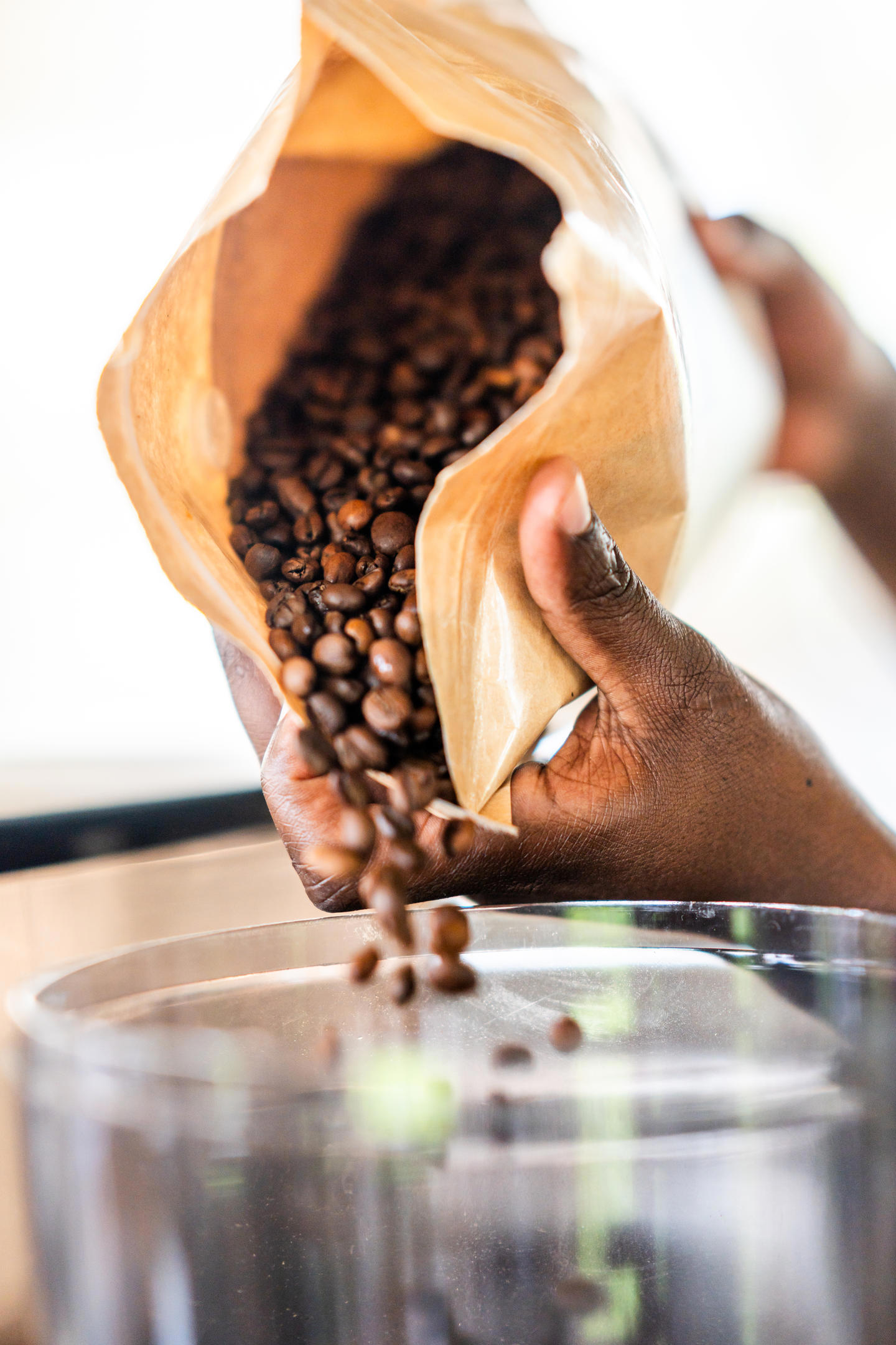 Man pouring roasted coffee beans from a brown paper bag into a grinder