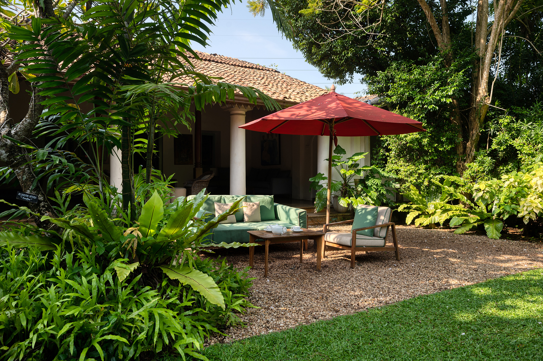 Comfy lawn furniture set outside a bungalow under a red umbrella surrounded by greenery