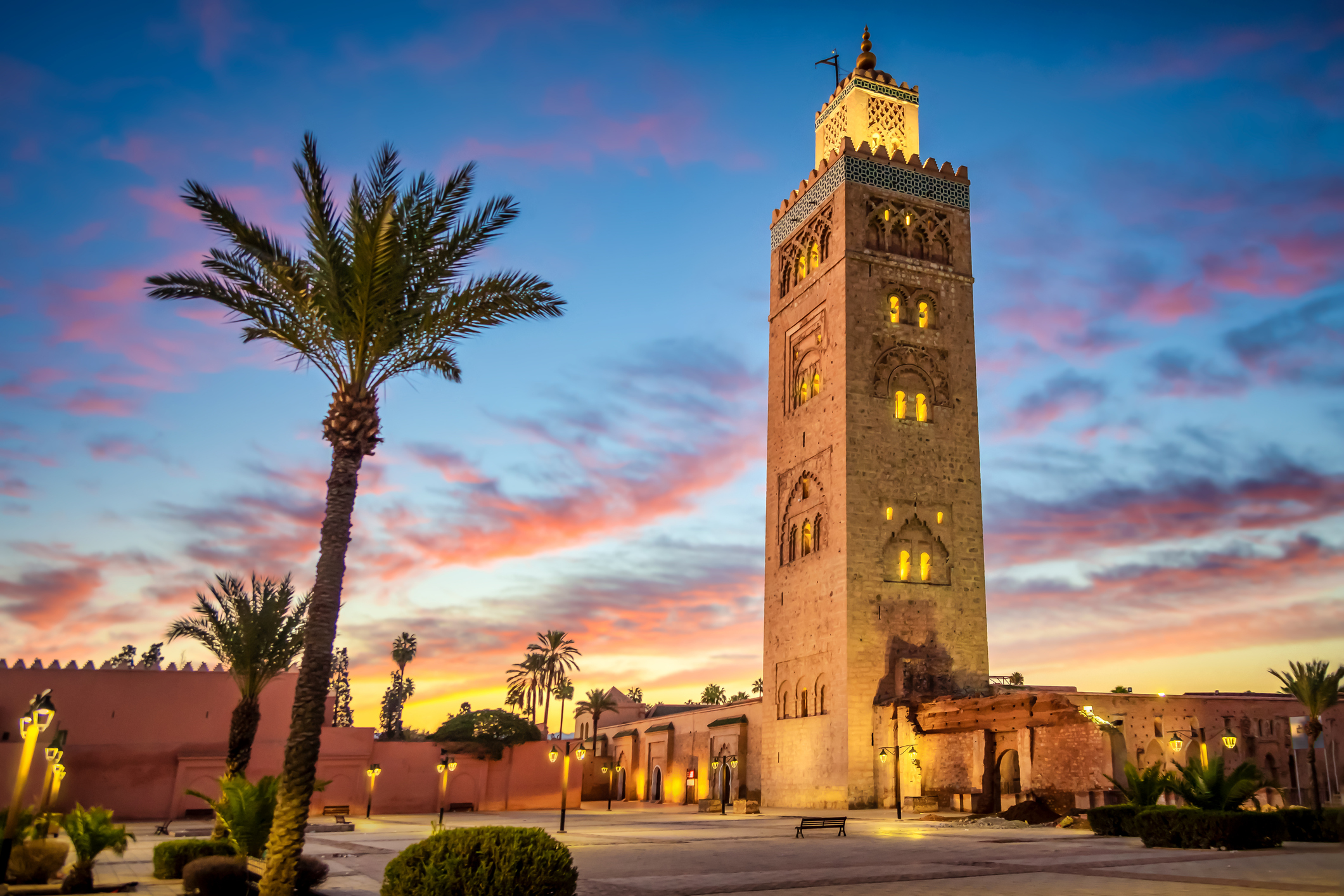 A view of Koutoubia mosque in Marrakech surrounded by palm trees as the sun sets
