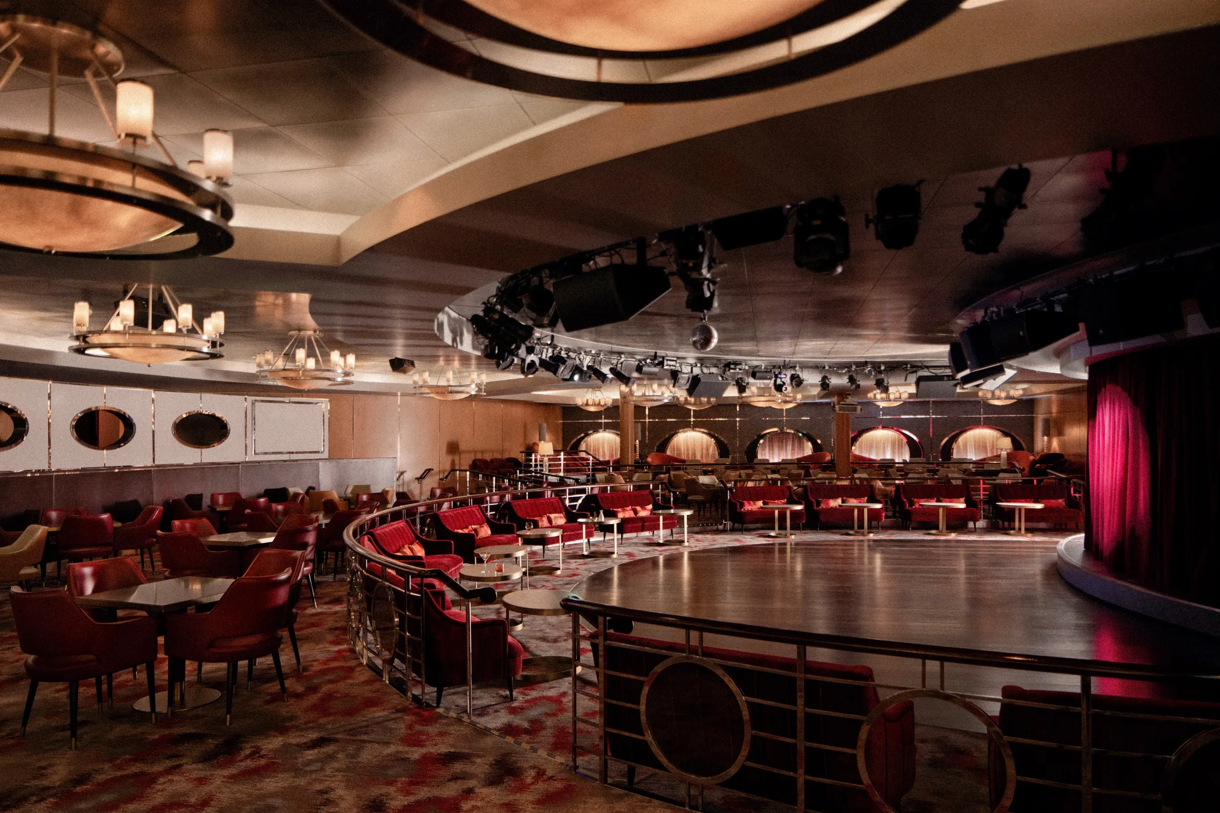 Elegant Crystal cruise ship theatre and lounge with red seats, round tables, and a grand stage framed by red curtains.