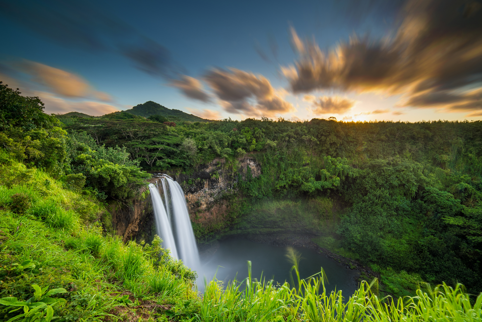 A picturesque waterfall in Kauai, illuminated by the warm hues of a sunset sky.