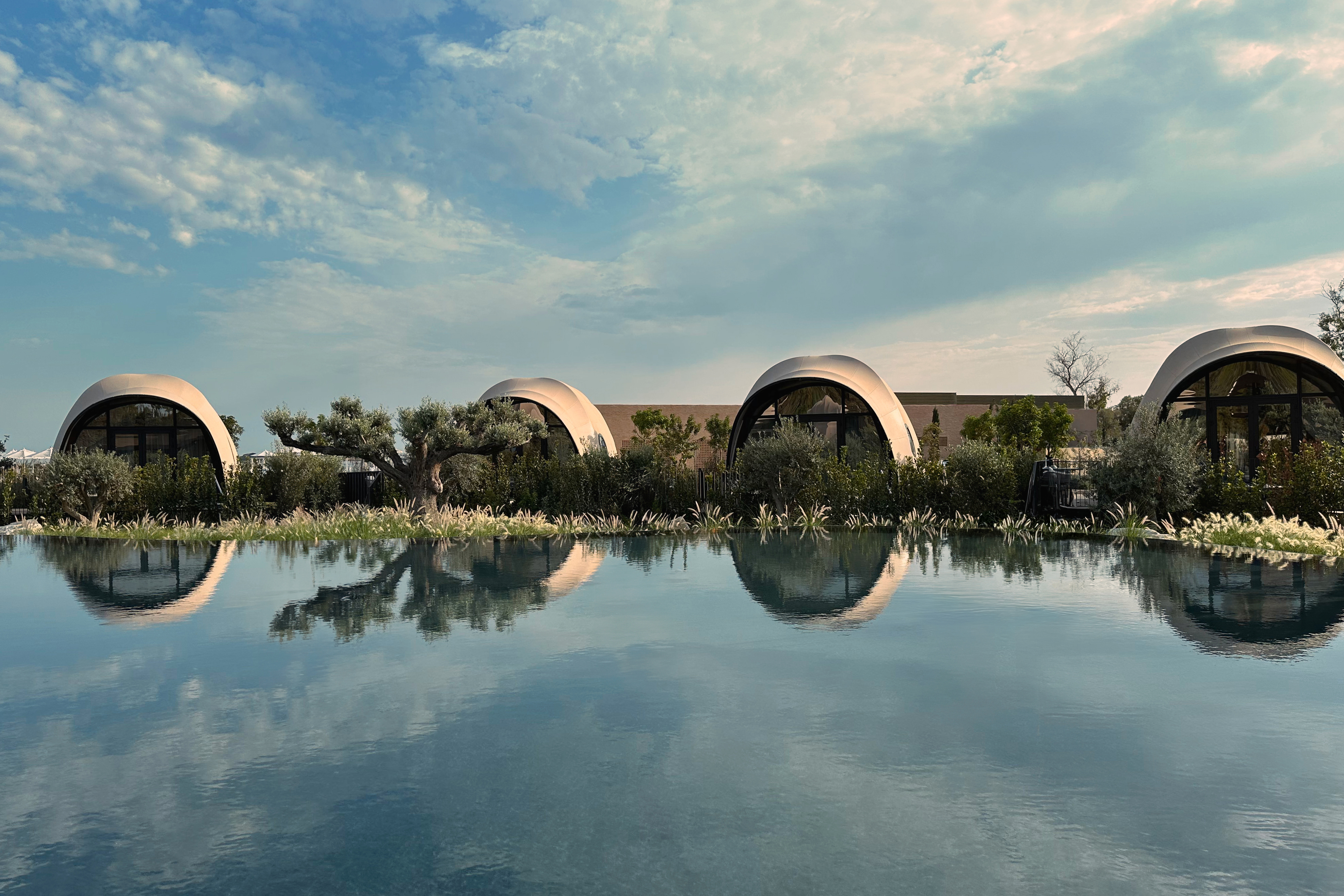 Four domed luxury tents surrounded by greenery by a lake 