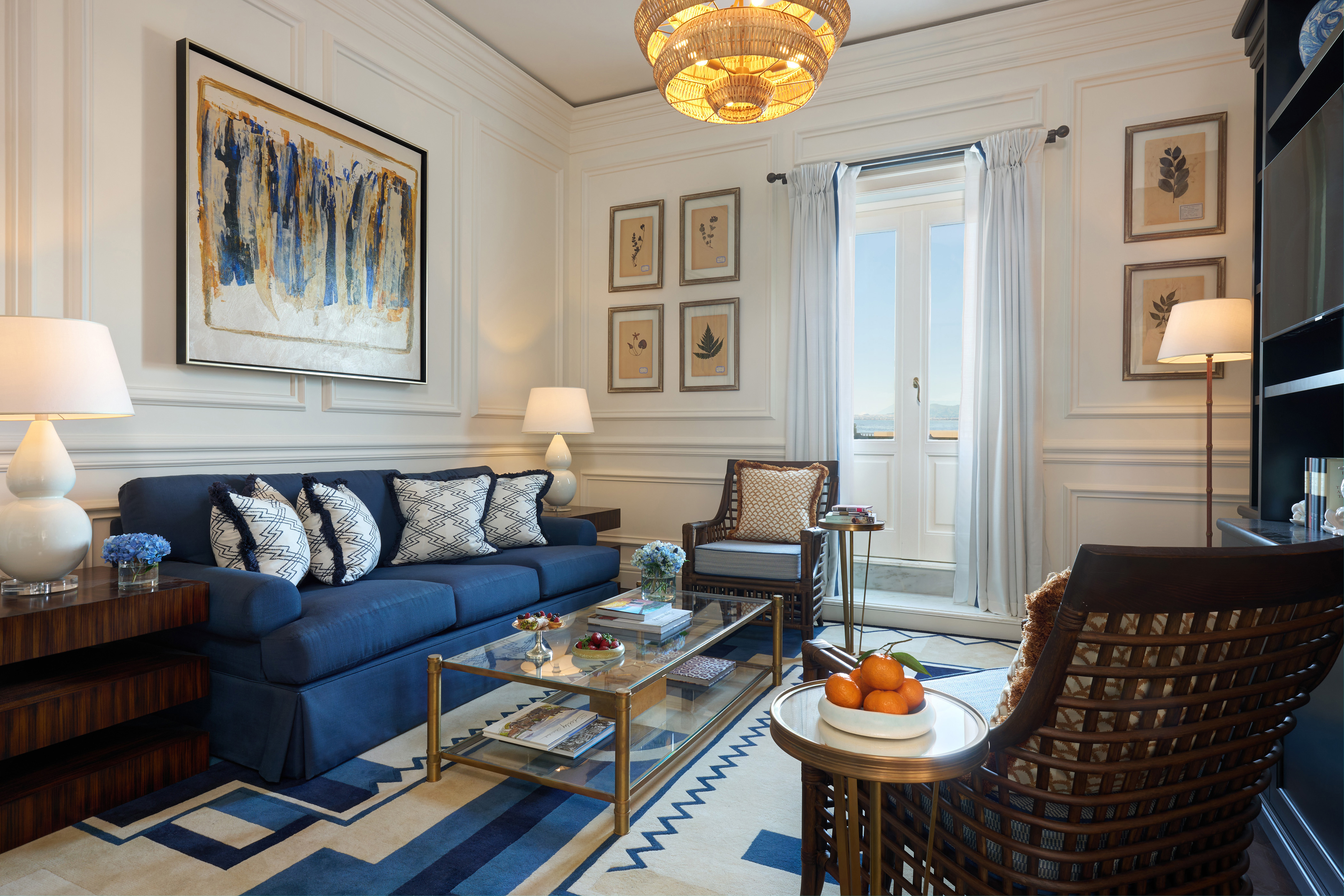 A finely decorated living room with a blue sofa, patterned armchairs, a glass coffee table, and various artworks on the walls.