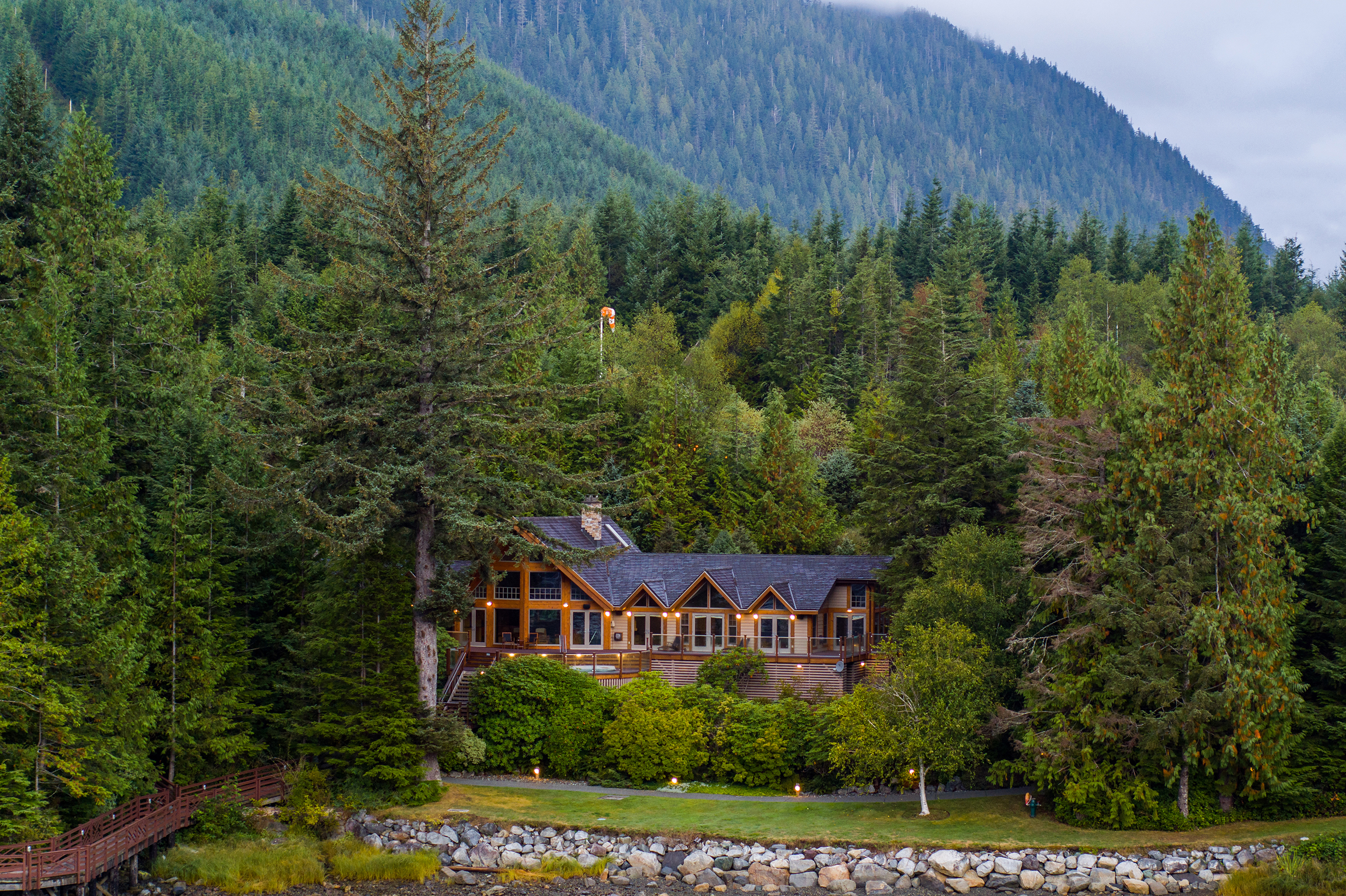 A grand wooden lodge poking out from among tall green trees with mountains behind