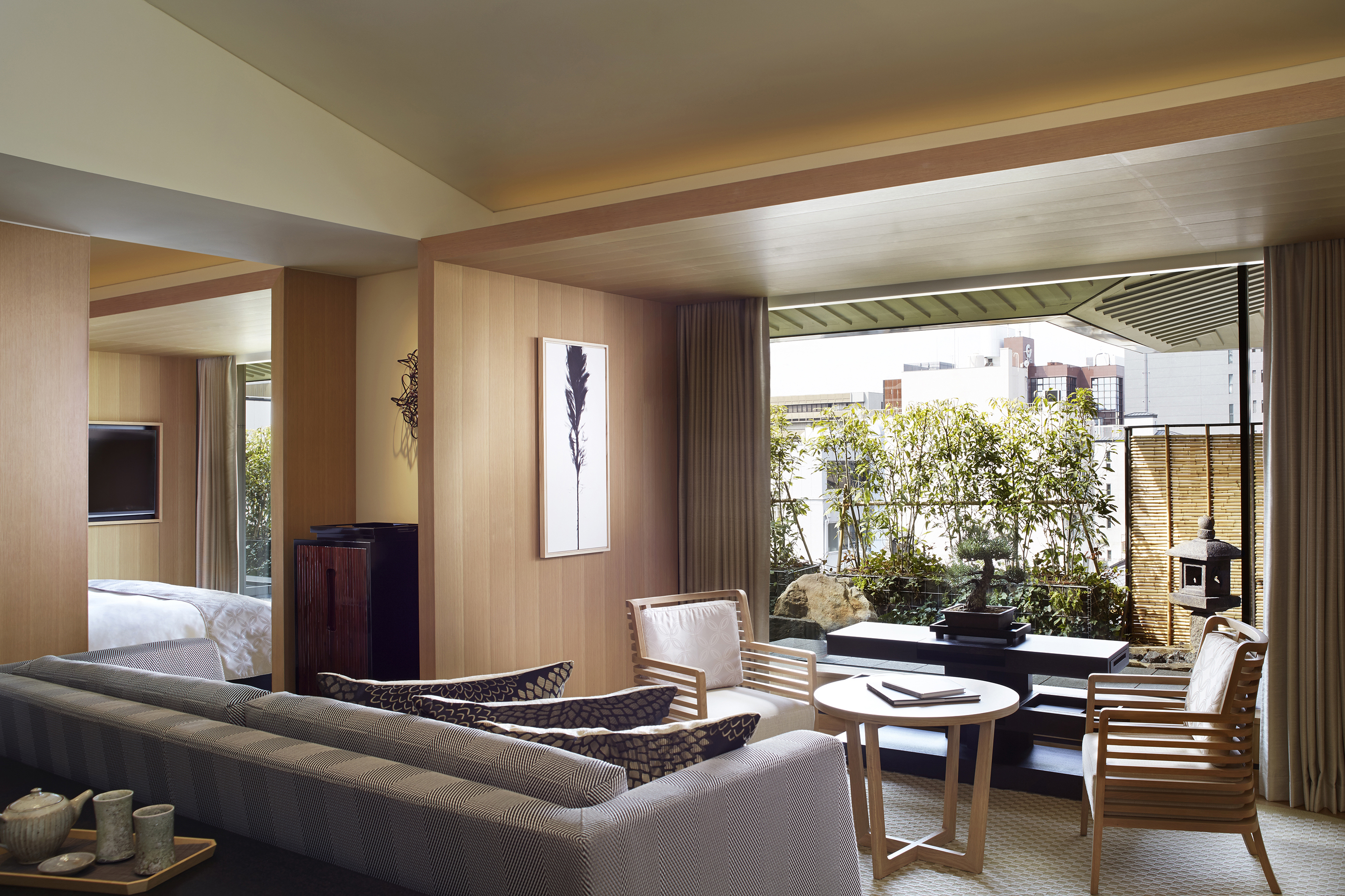 A modern suite featuring pale wood decor and furniture with a comfy sofa, dining area and large window overlooking a garden