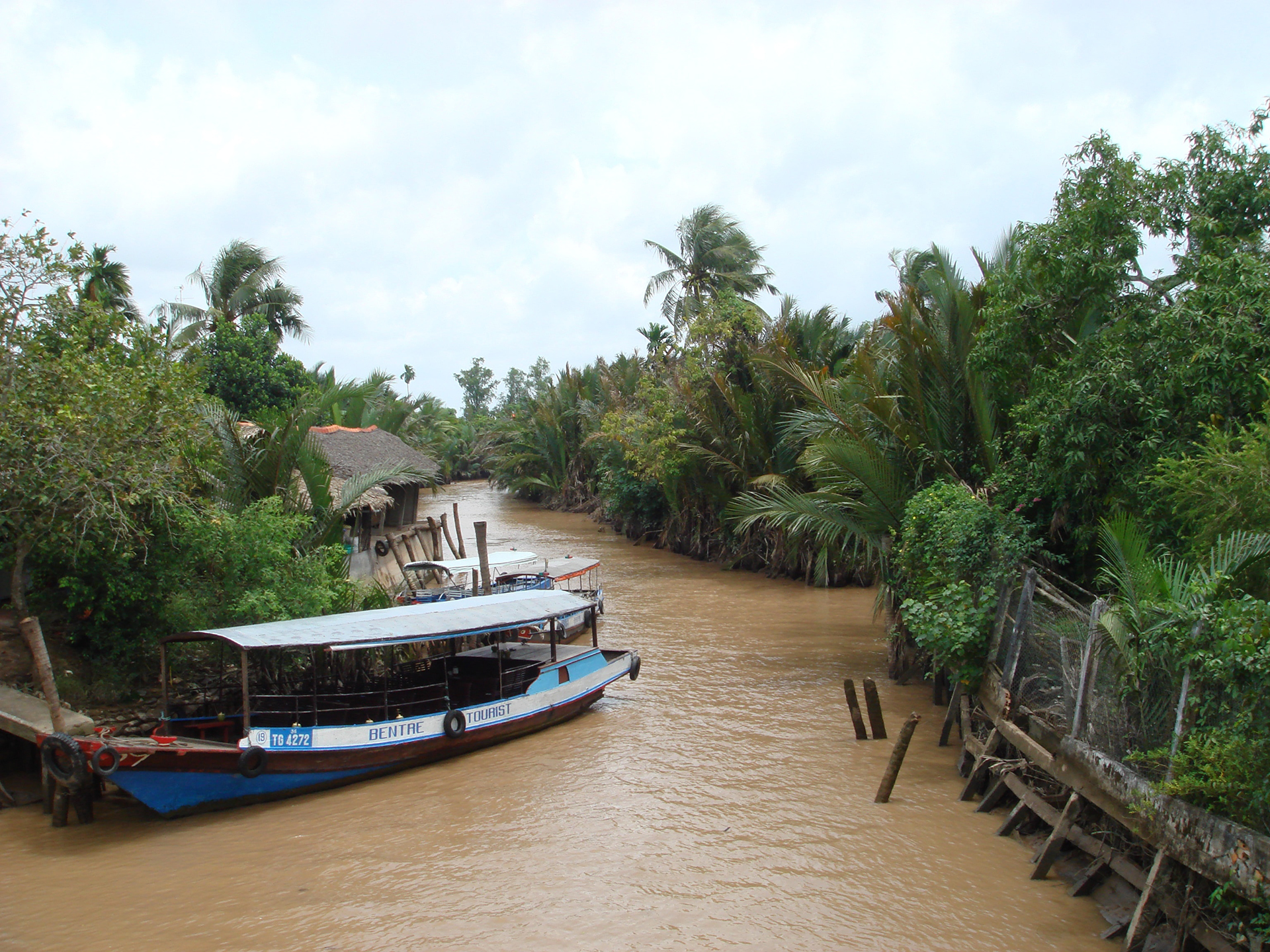A blue river tourist boat docked on a brown muddy river
