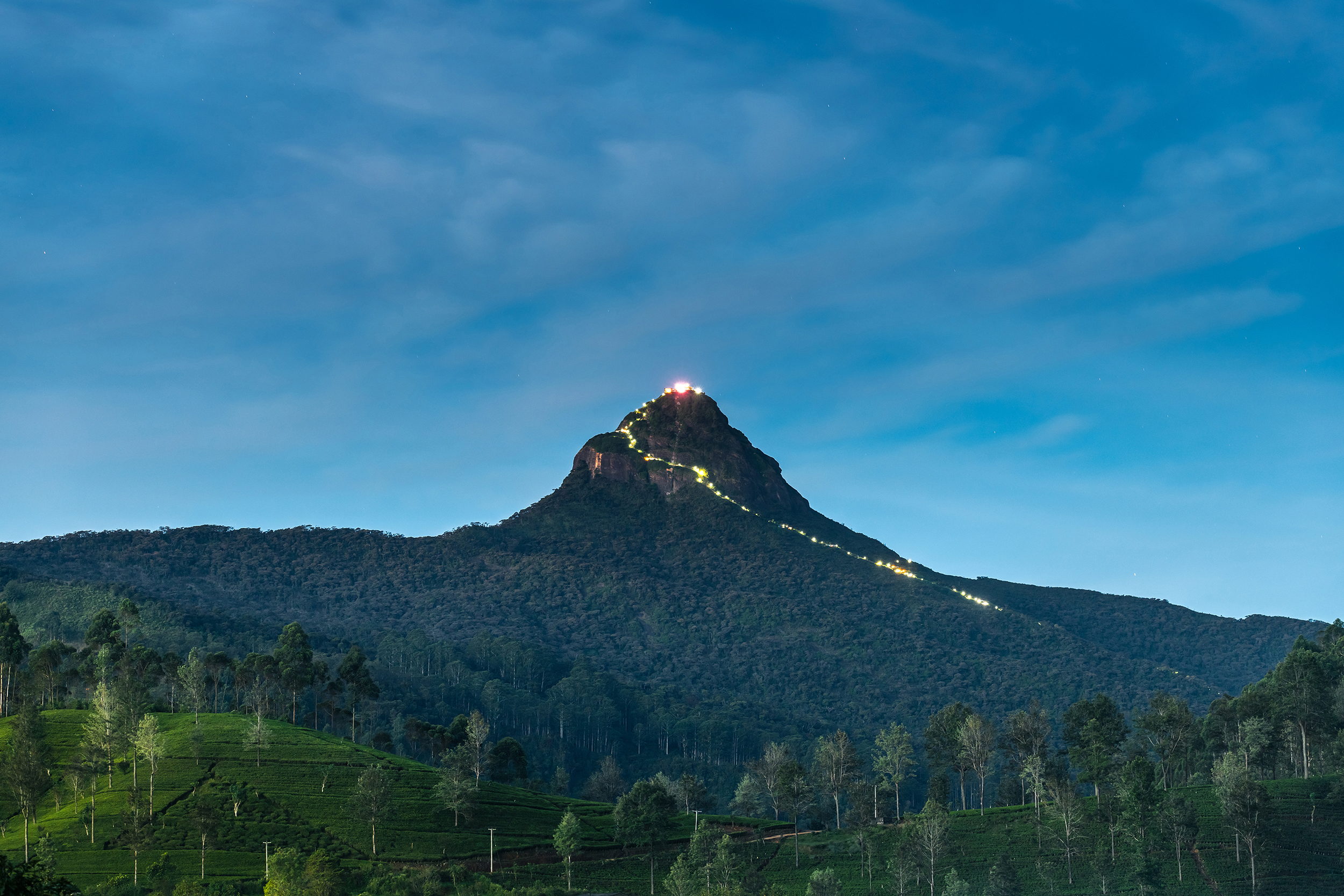 Large mountain in low light with a line of lights twisting up its side to the summit