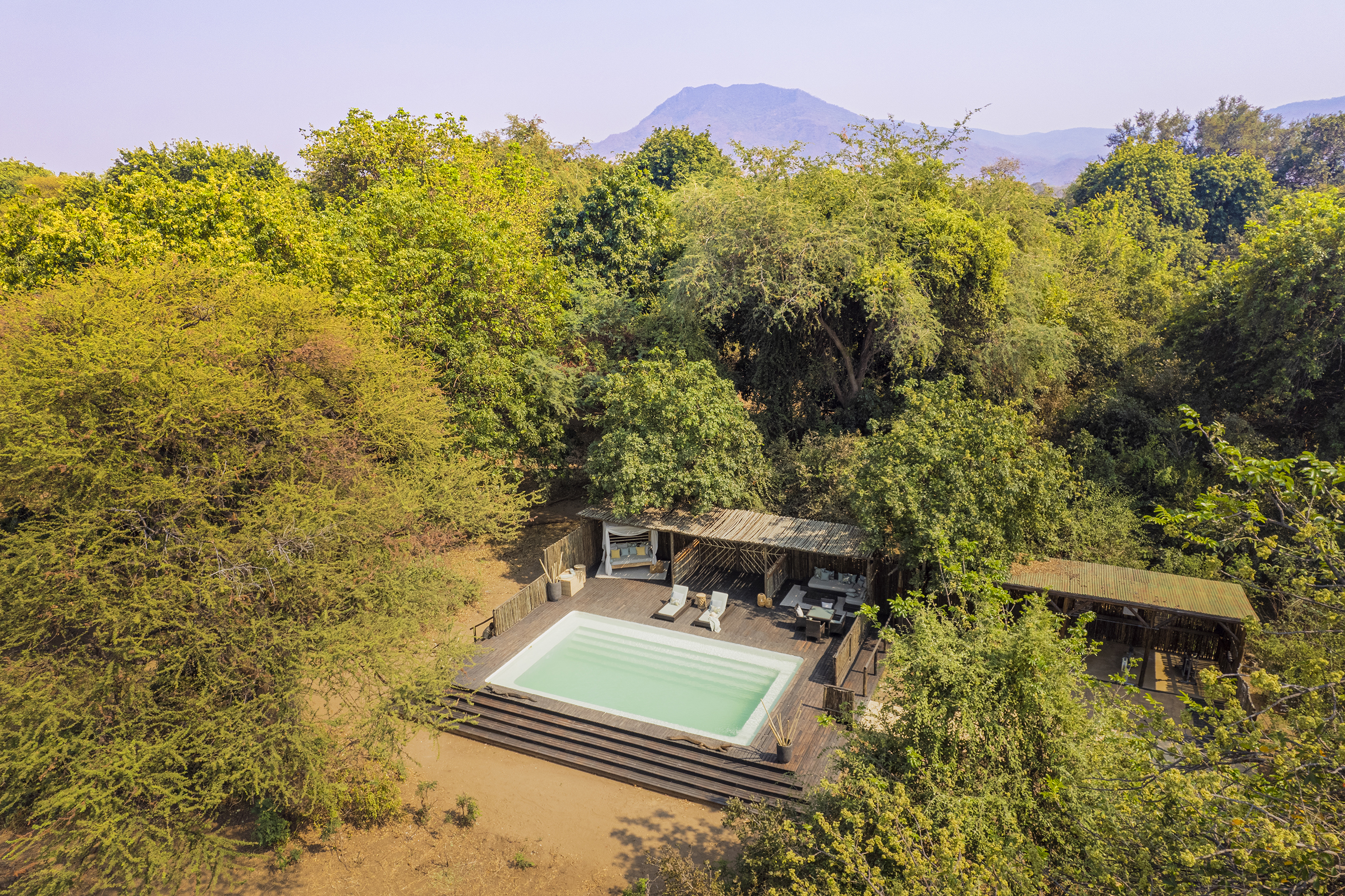 The raised pool deck of Chiawa Camp surrounded by dense trees and backed by distant mountains
