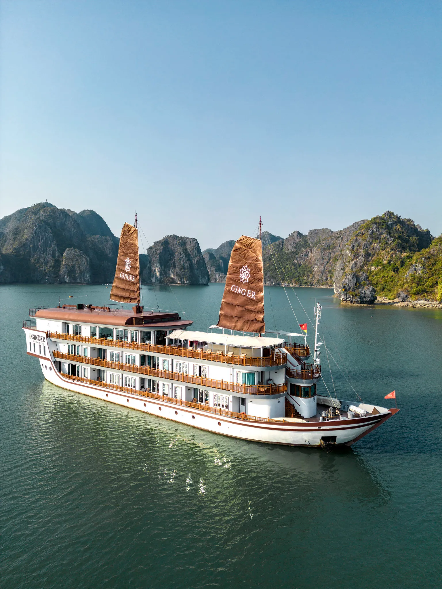 Heritage Line’s multi-deck cruise ship 'Ginger' sails through a calm bay surrounded by rocky, green islands under a clear blue sky.