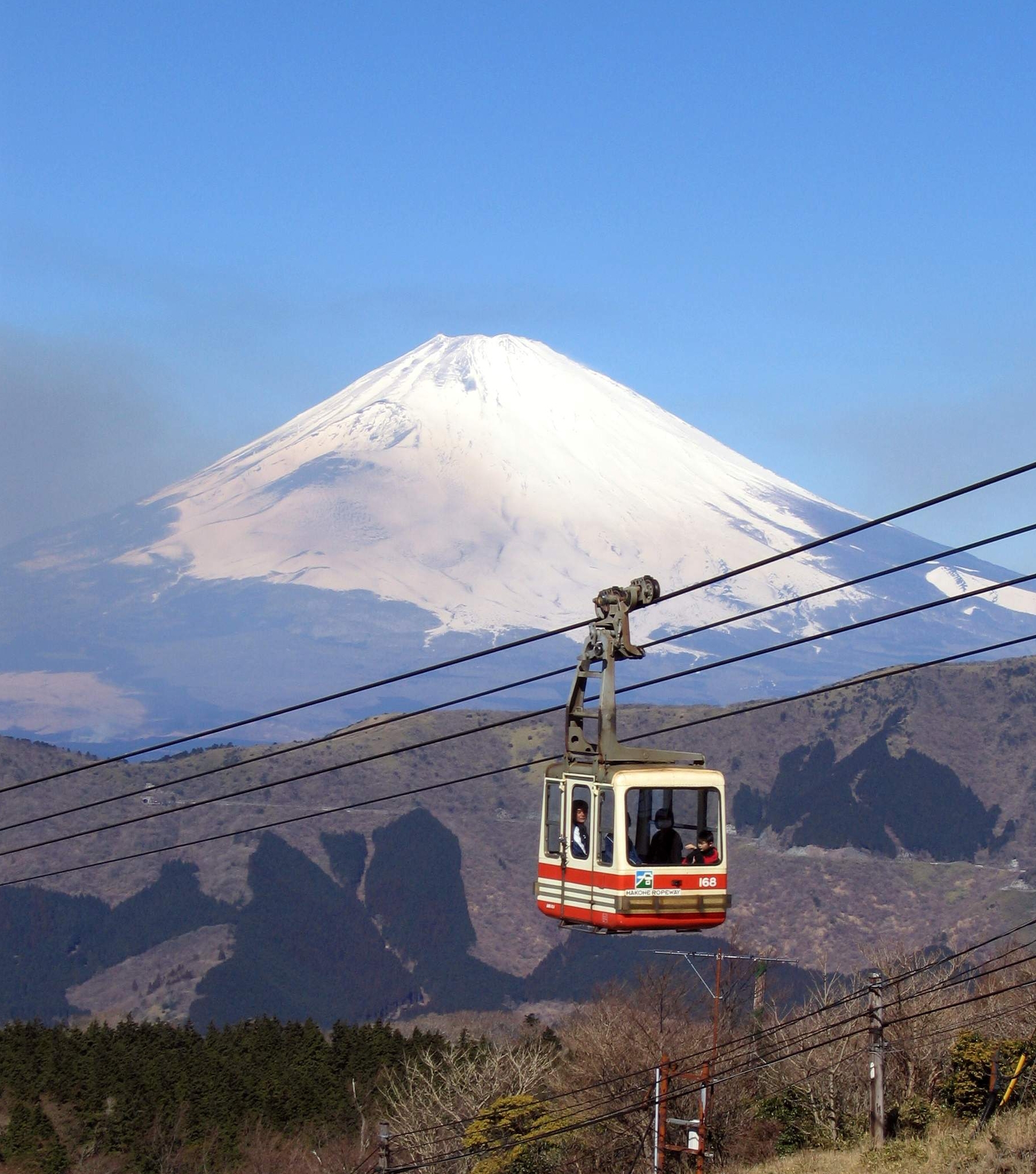 A view of the Hakone ropeway cable car ascending in front of a snow-capped Mount Fuji