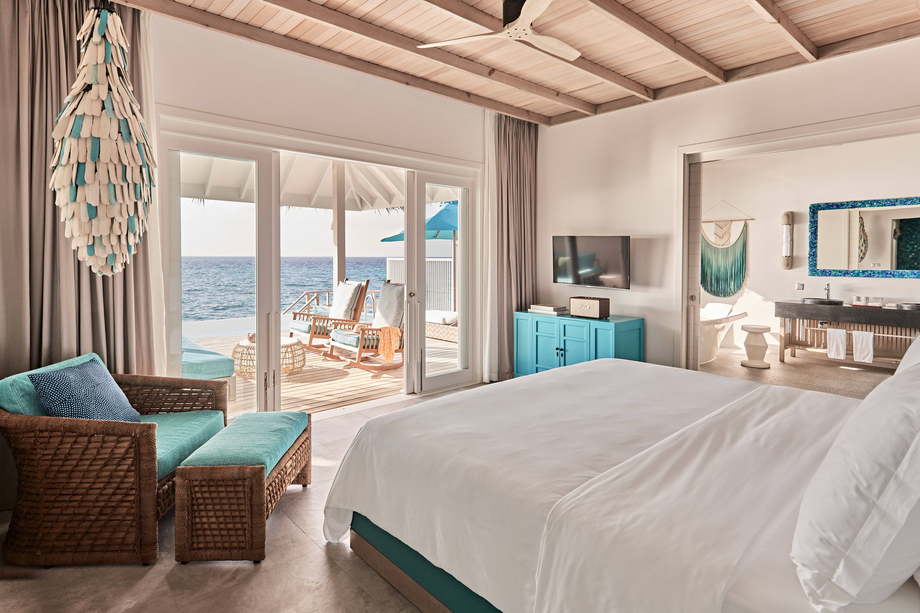 A coastal style bedroom at Finolhu with blue and white decor and a bed facing doors leading onto a pool deck