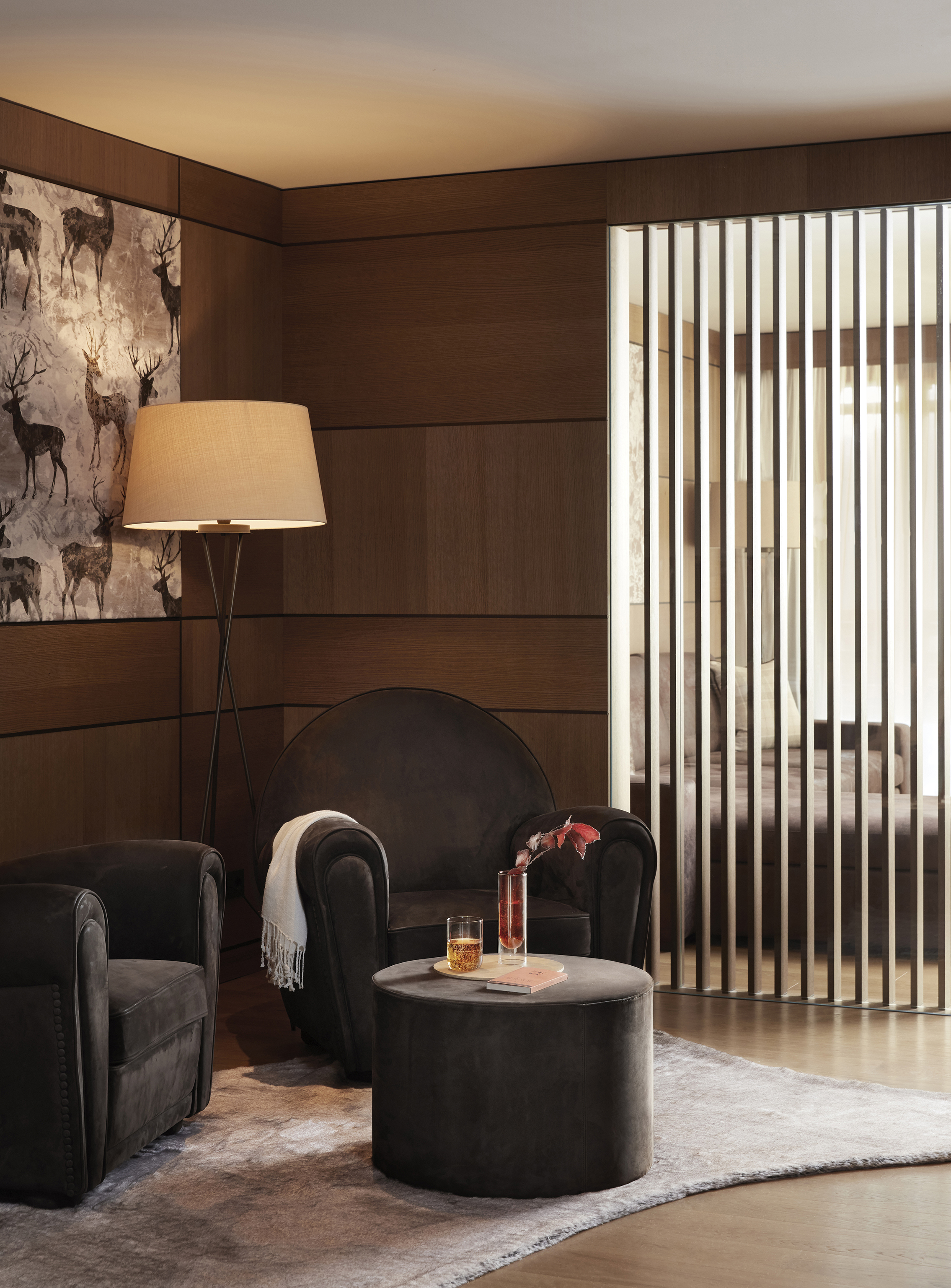 Lounge area of exclusive spa suite decoration with two dark plush chairs, reindeer artwork and a coffee table with whisky tumbler on top