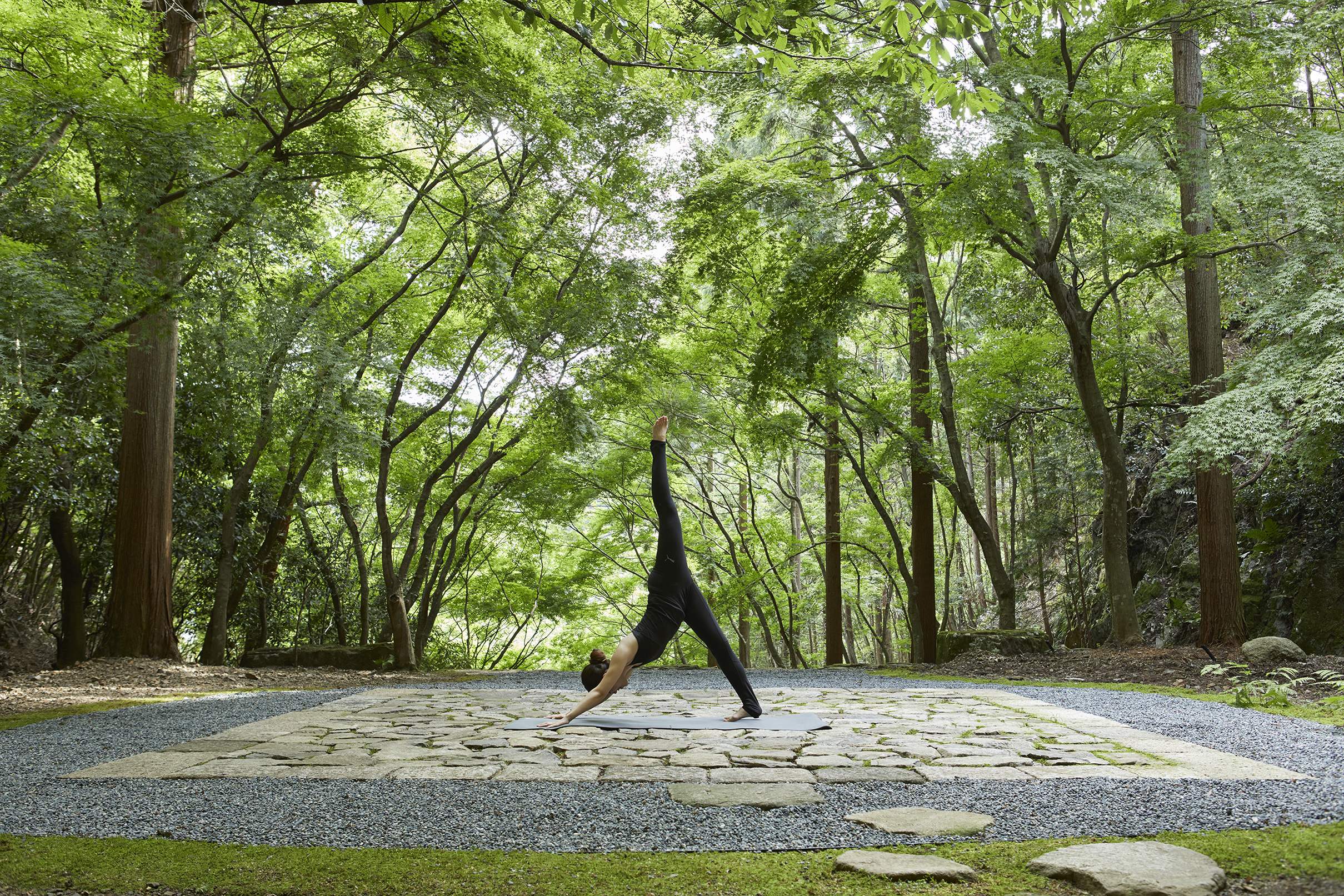 A woman practicing yoga on a stone patio in the Temgamine Garden beneath green trees