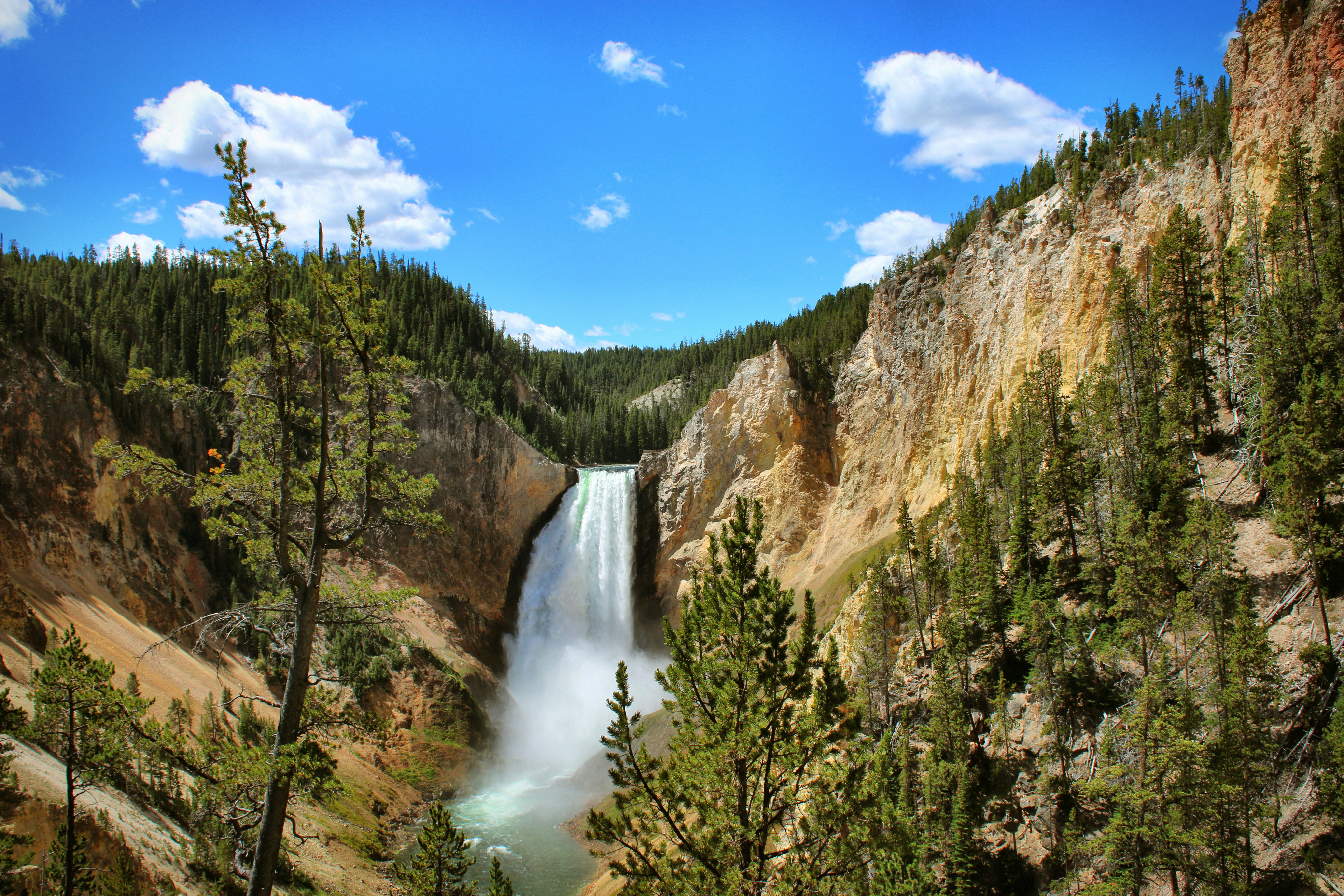 A waterfall surrounded by trees beneath a clear blue sky dotted with white clouds