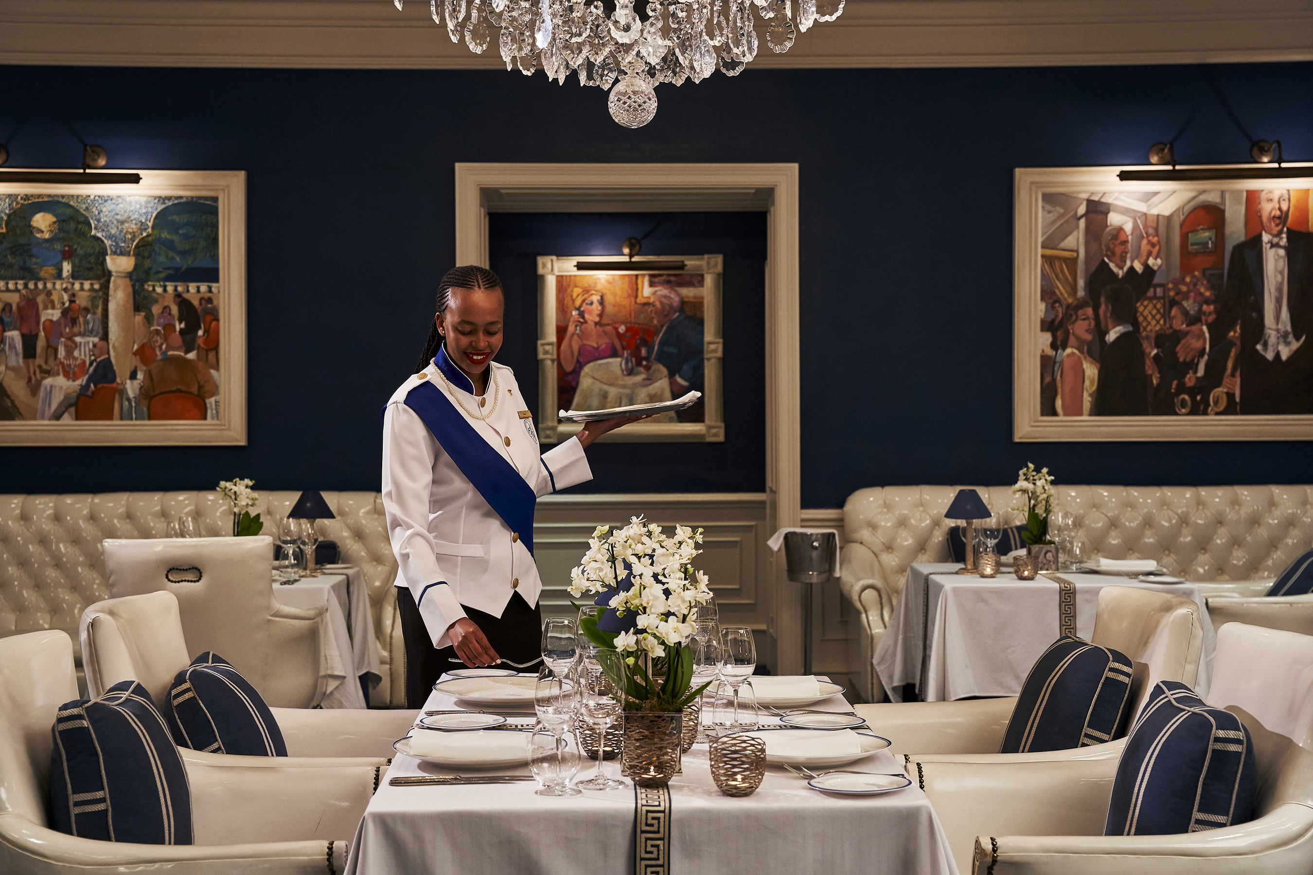 A smiley woman setting a table for dinner in the elegant Grill Room at The Oyster Box with art work on the walls