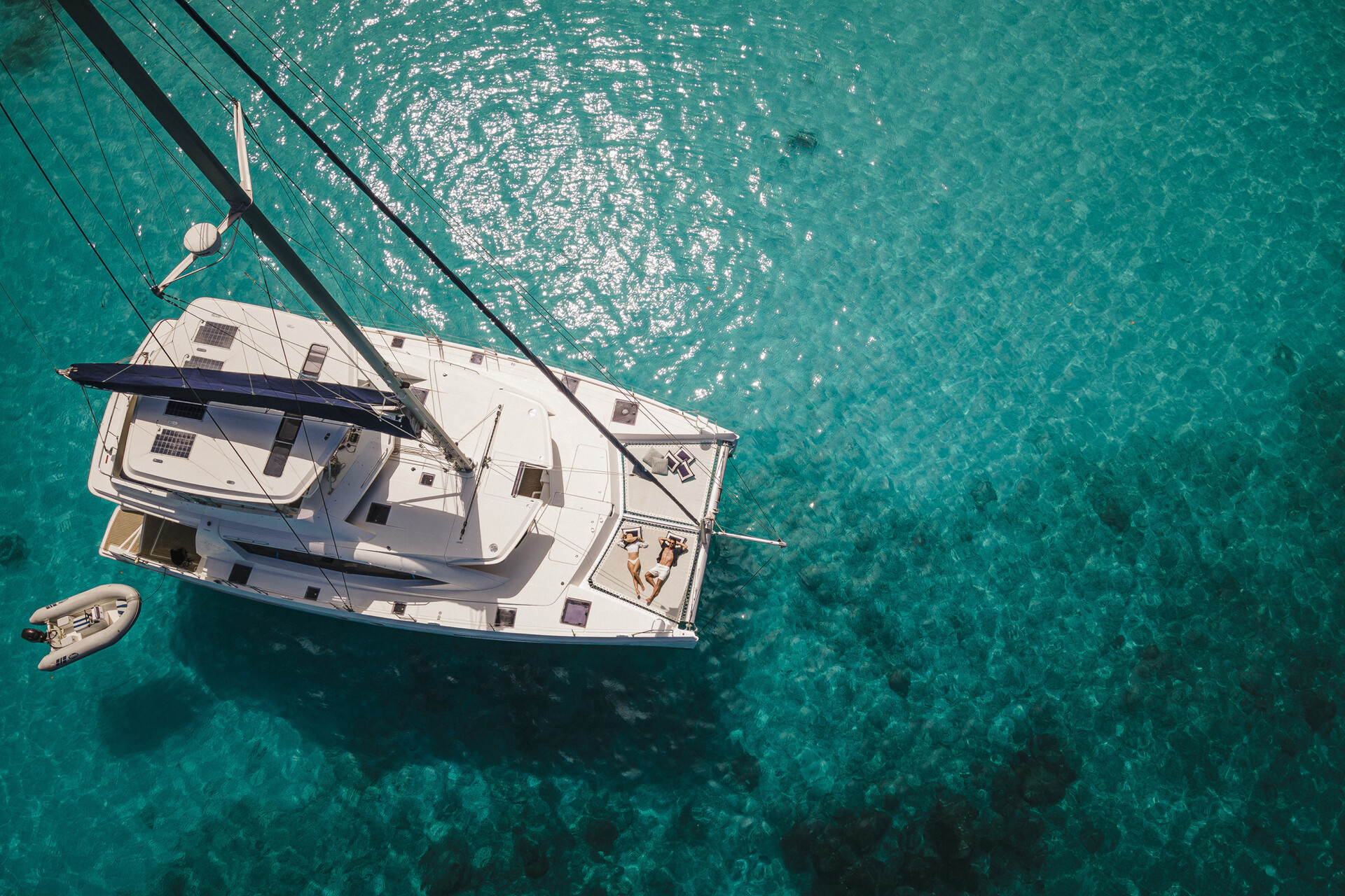 Couple lounging on deck of a catamaran anchored in the bay