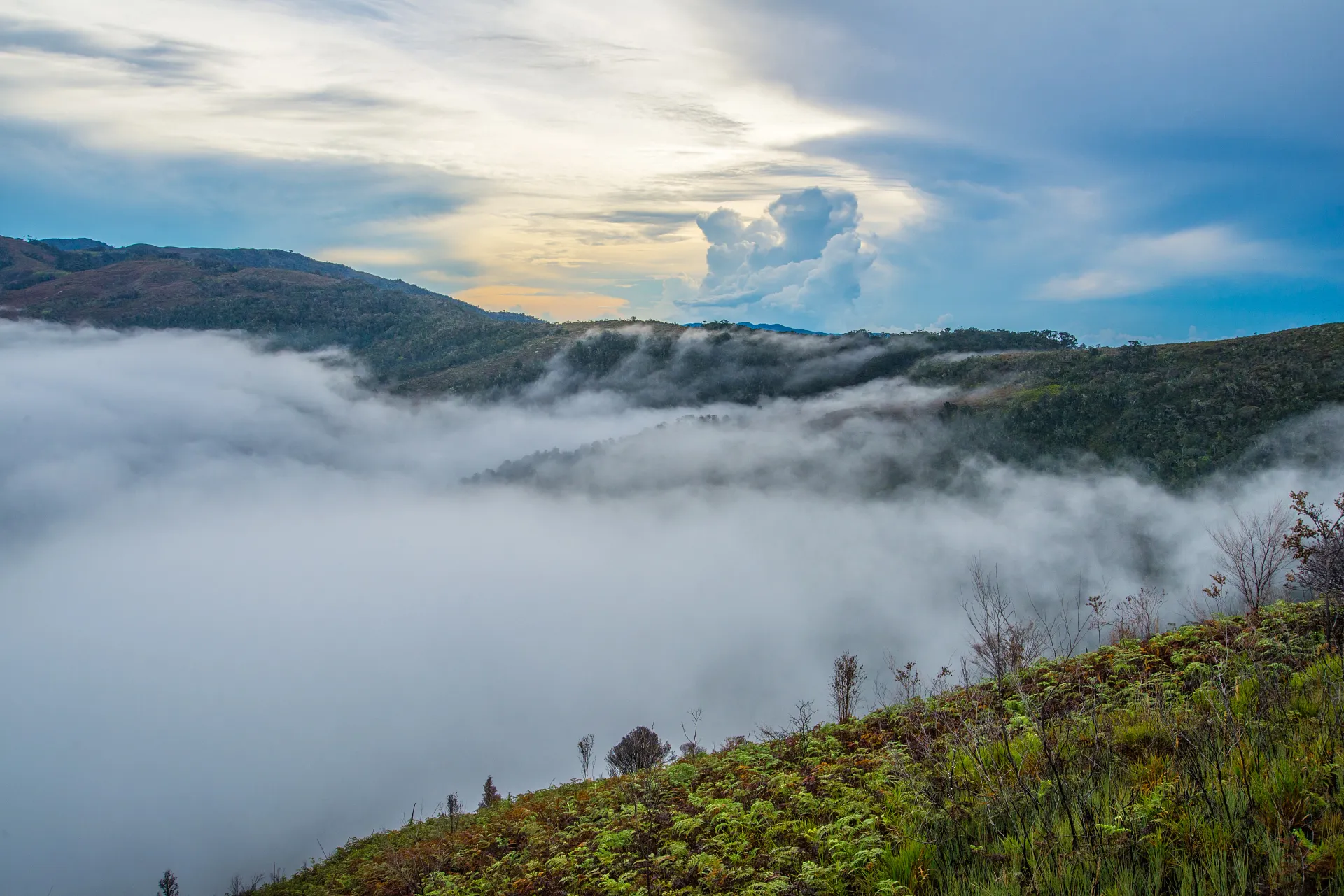 Scenic mountain landscape with fog-covered valleys under a partly cloudy sunset sky.