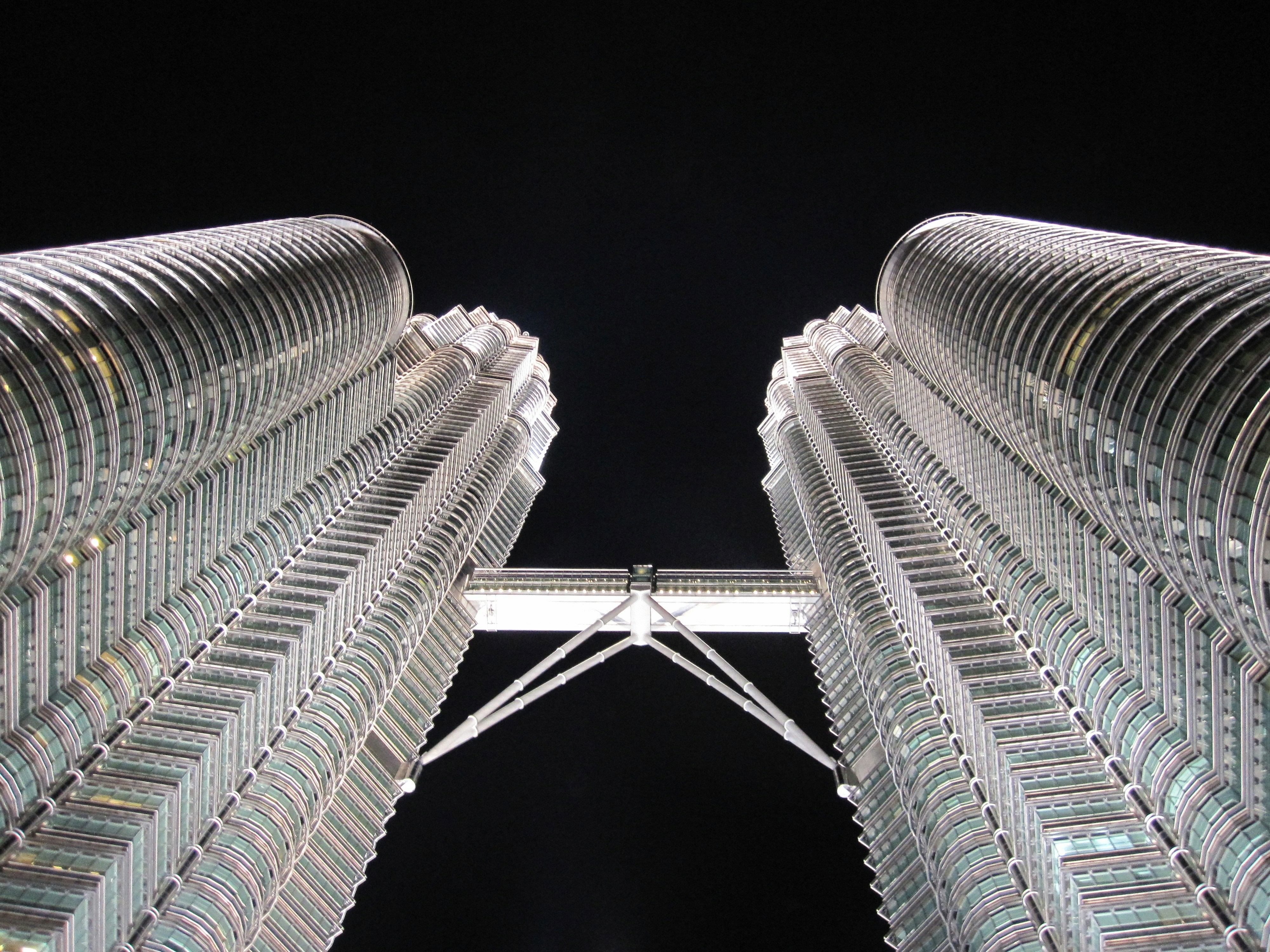 A ground view of the petronas towers and skybridge in Kuala Lumpur lit up at night and soaring into a black sky