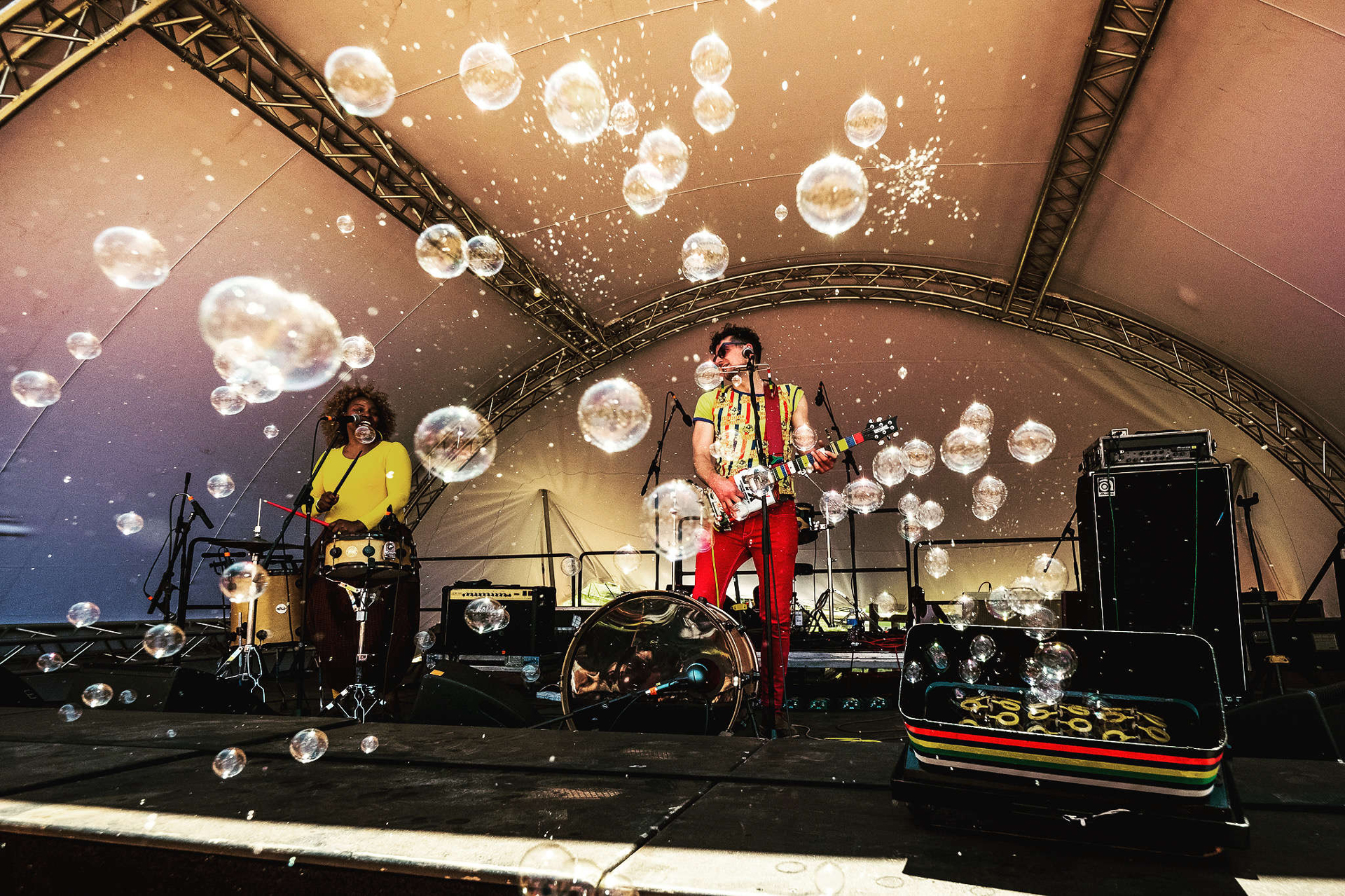 Two people on a stage performing music with bubbles passing in front of the camera