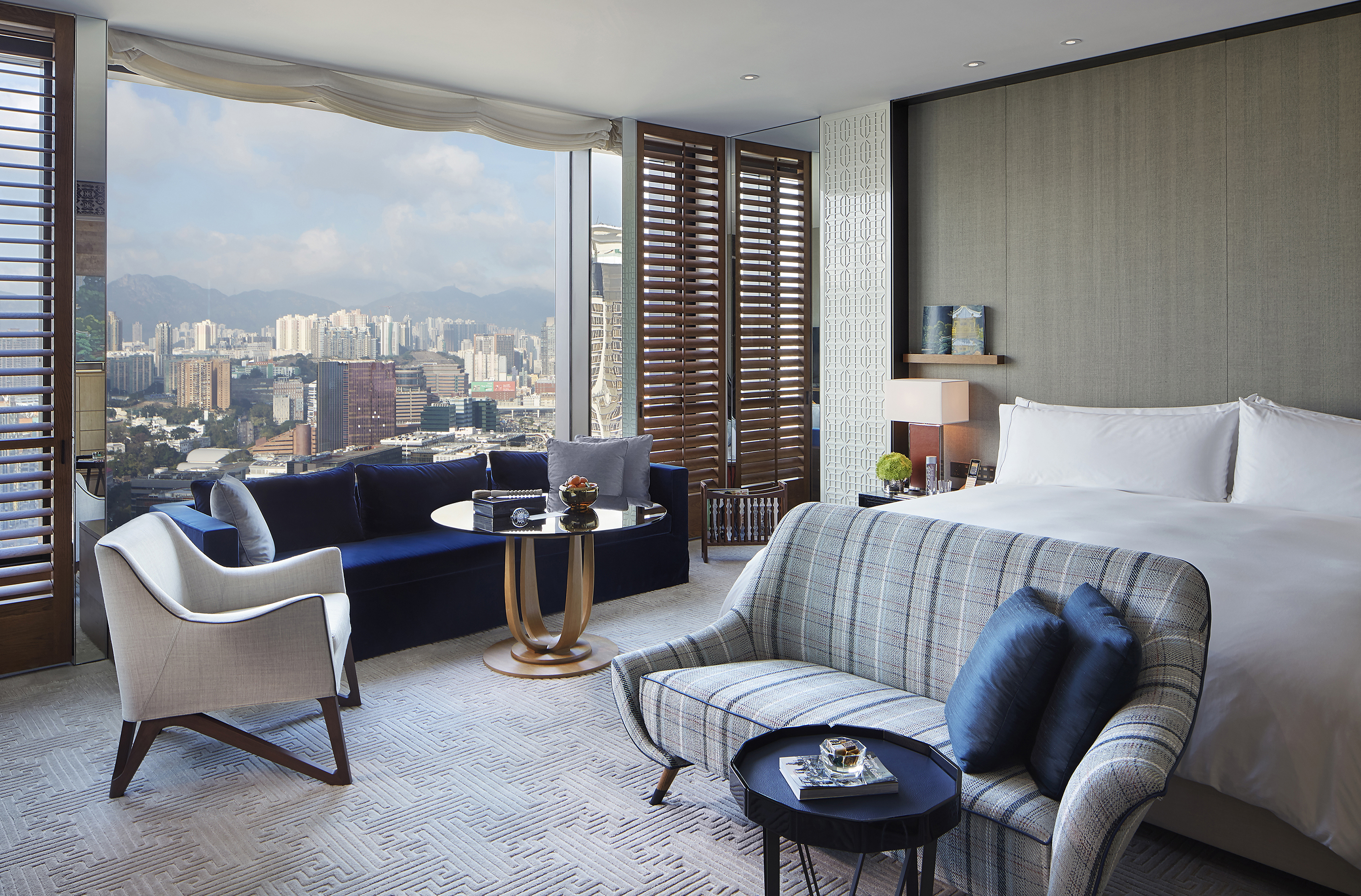 Kowloon King Room bedroom featuring patterned and solid colour furniture, wooden shutters and a large window with city views