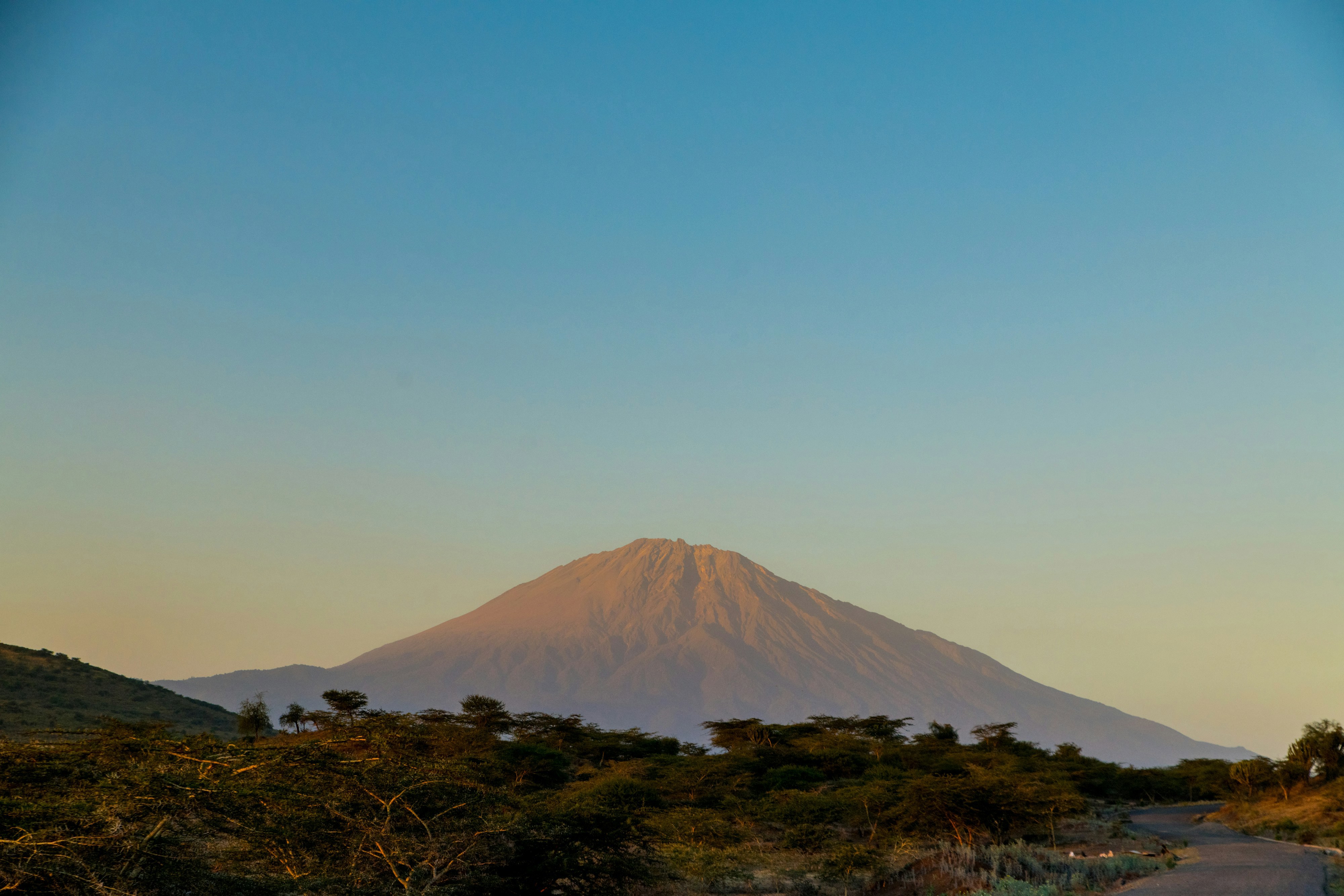 Mount Meru in Arusha, Tanzania under a clear sky with forests and a glimpse of a road in the foreground