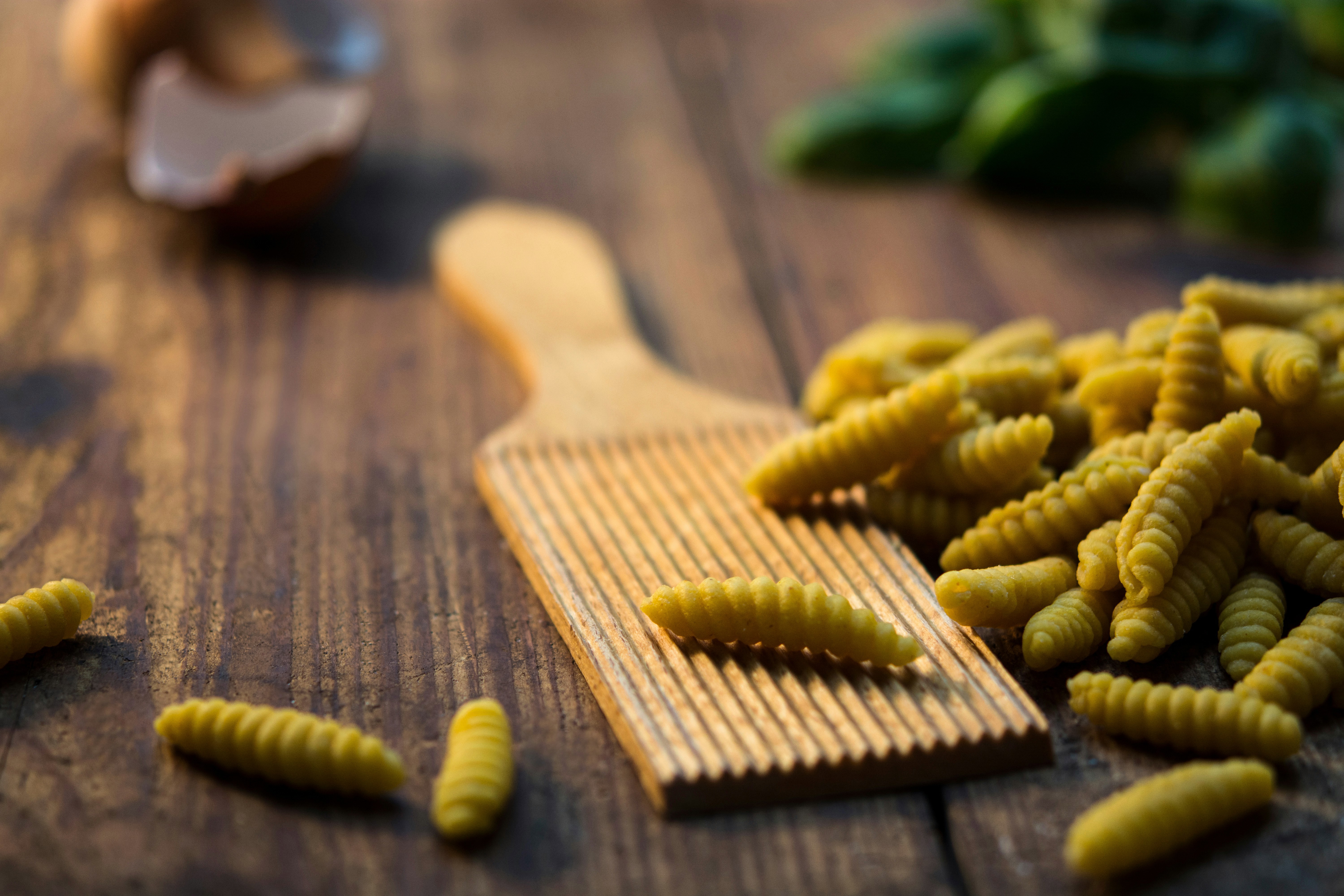 A ribbed pasta board beside a pile of fresh pasta on top of a wooden table