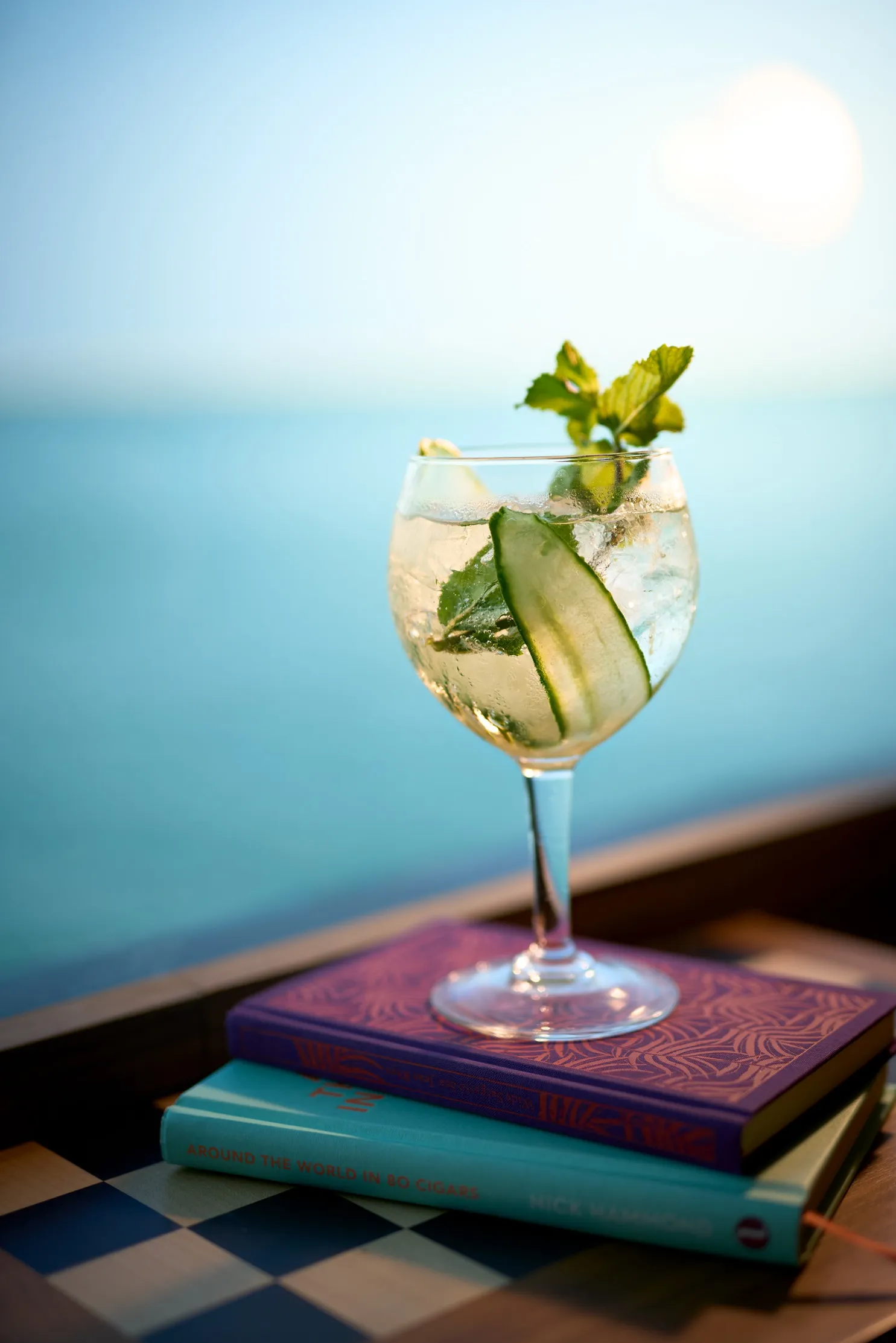 A refreshing cocktail with cucumber and mint on two books, set against a serene ocean backdrop.