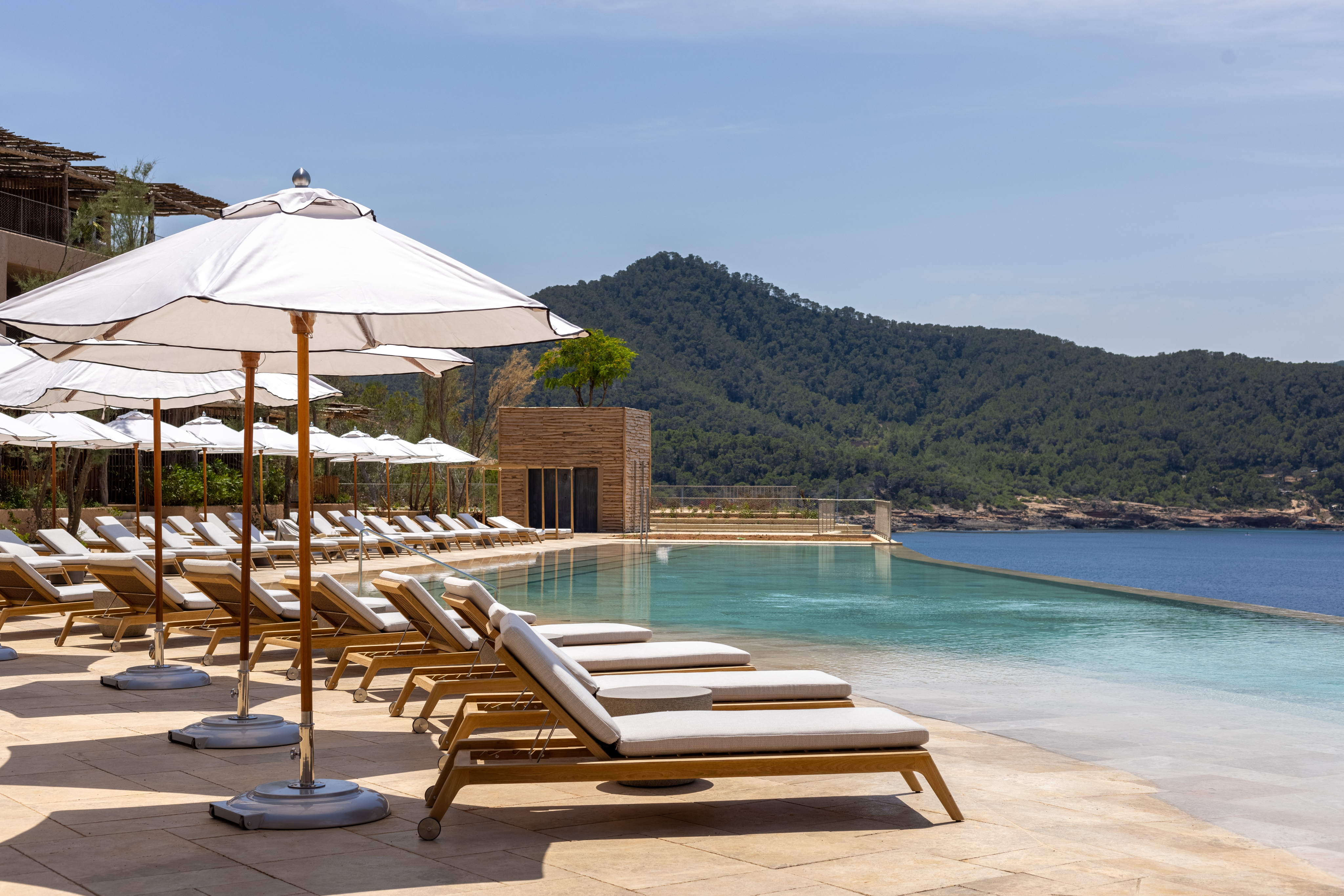 Luxurious outdoor pool area with lounge chairs and umbrellas overlooking mountains and ocean.