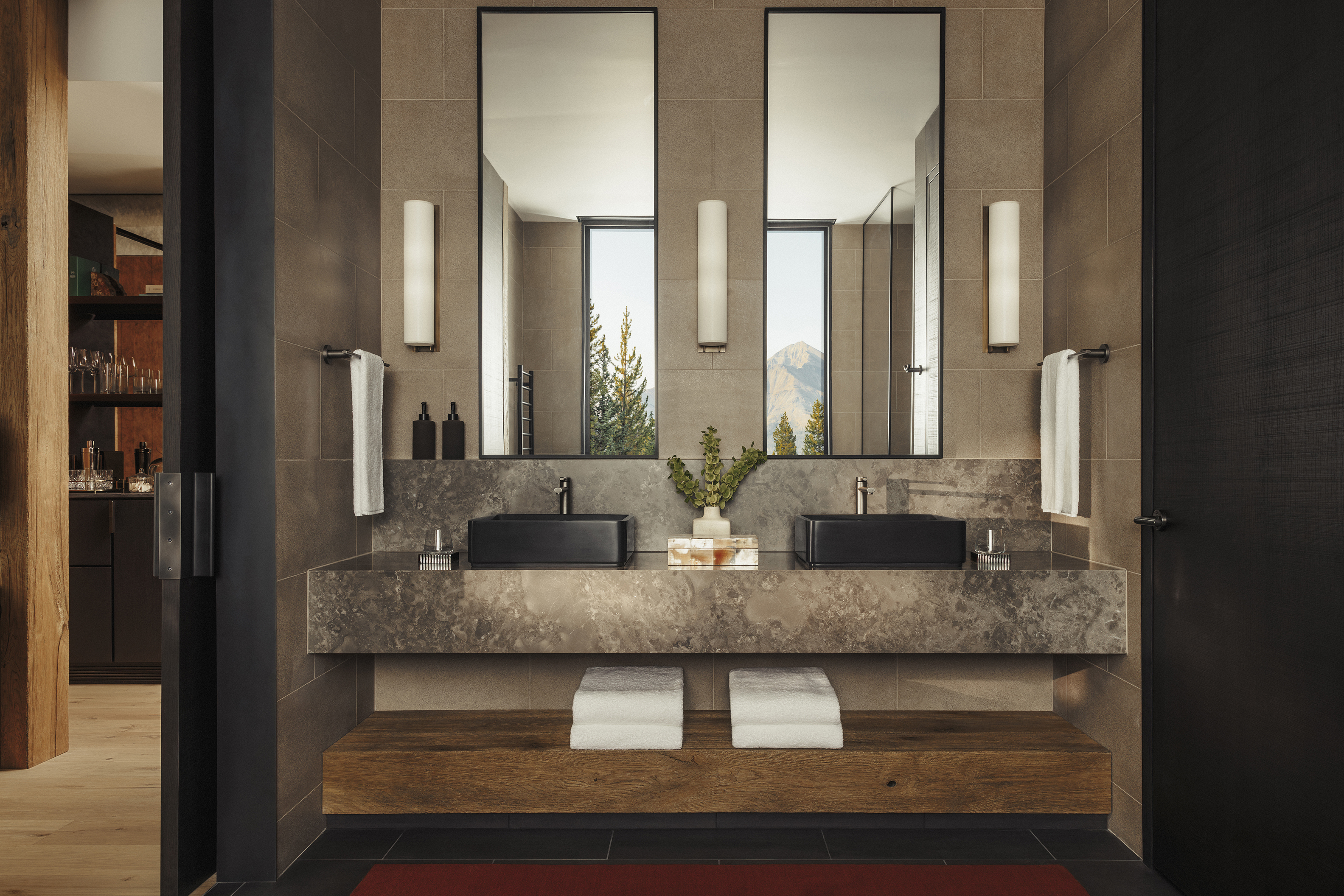 A double sink made of granite and wood below two mirrors reflecting the landscape 